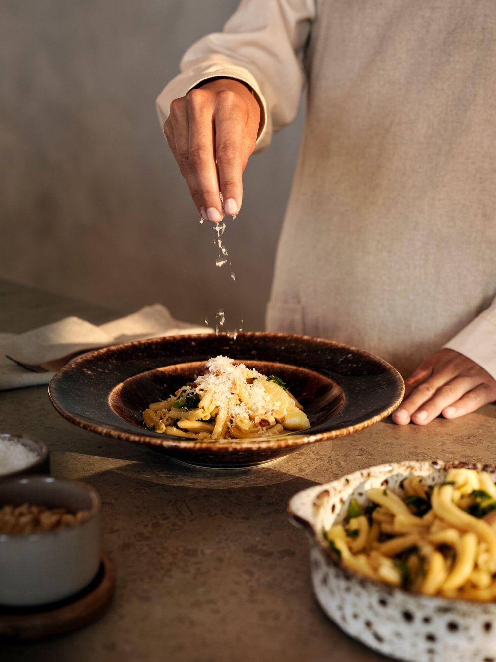 Chef finishing a gourmet pasta dish with fresh grated cheese, highlighting Dhoom’s plating techniques and fine dining artistry.