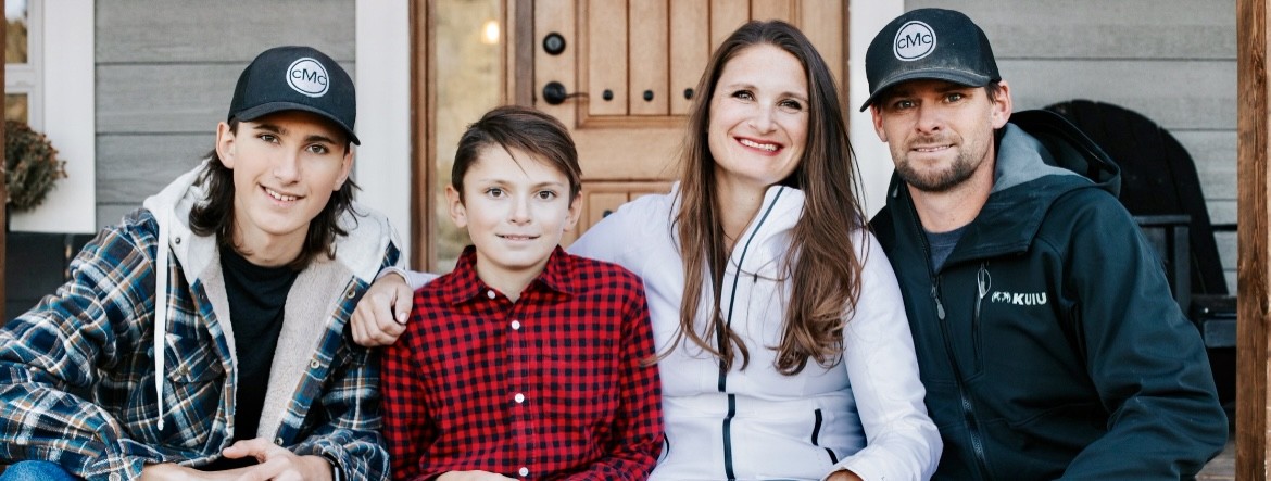 Anne, Chad and their two sons seated outside a wooden front door