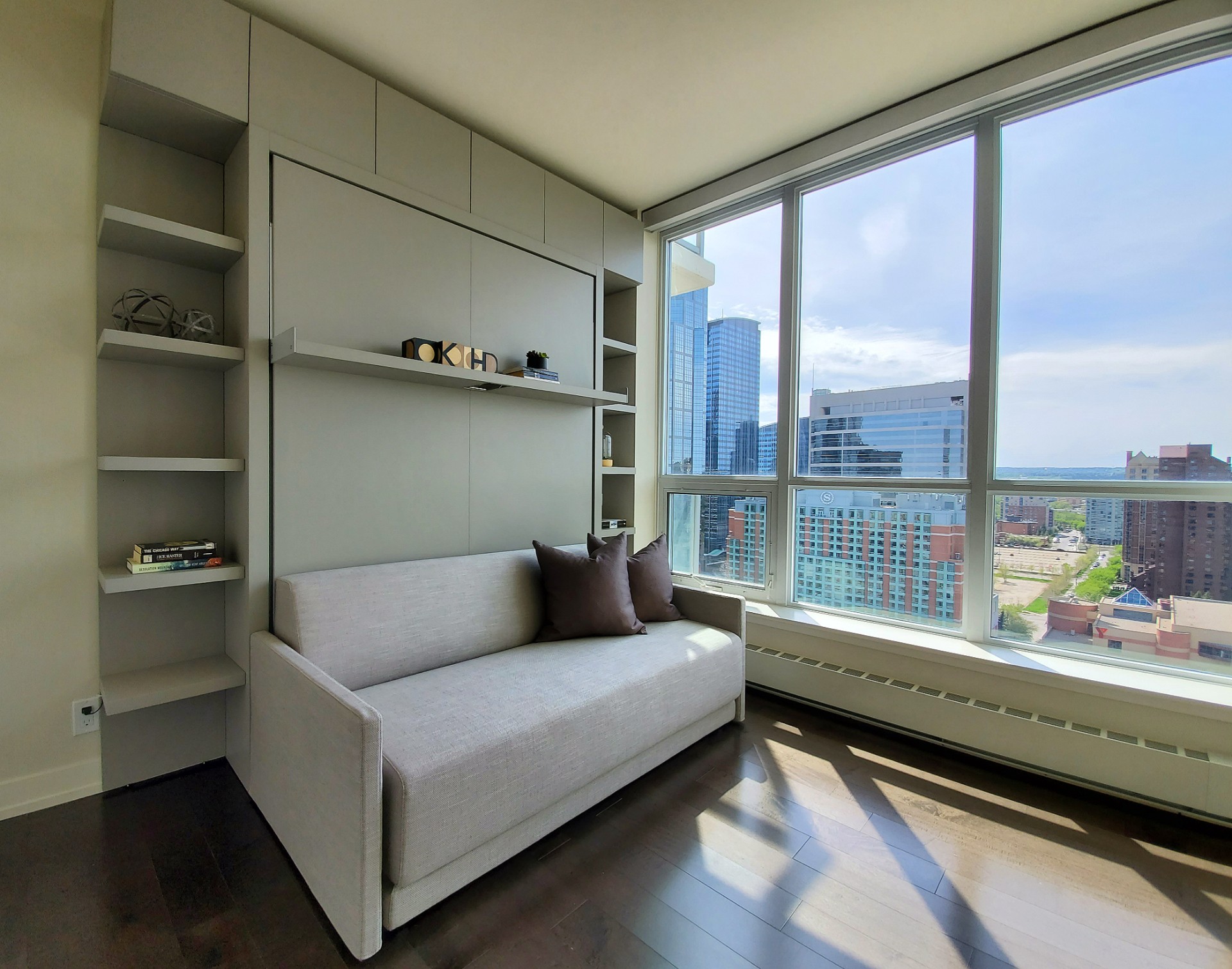 Image of KHD Homes design-build interior with built-in shelving, sofa, and large window overlooking cityscape with modern furniture.