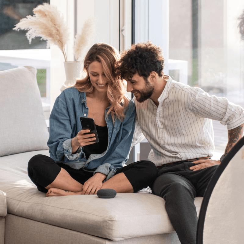 Couple with smartphone and smart speaker on couch.