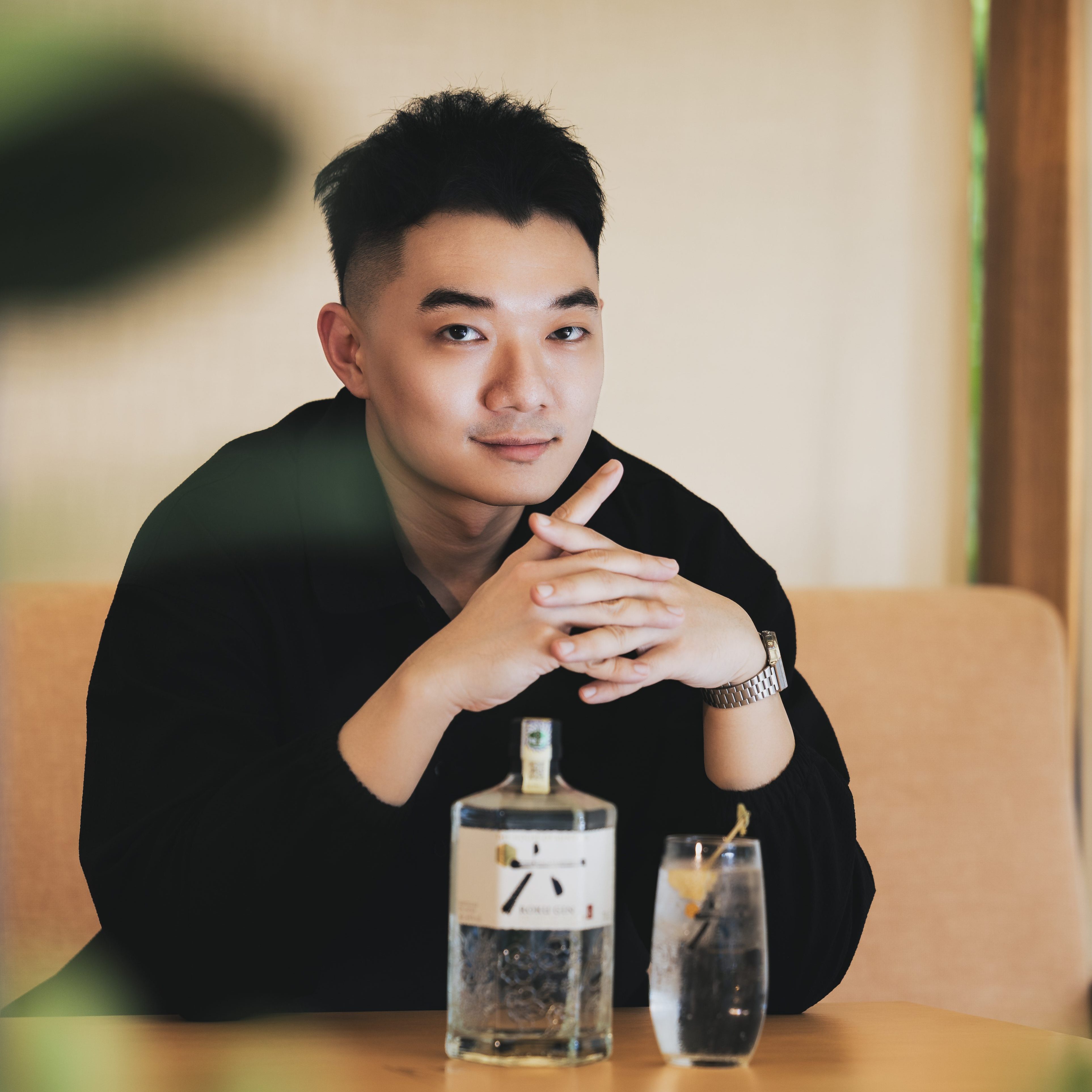 A person sitting at a table with a bottle of Roku Gin and a glass containing a cocktail, displaying a relaxed and inviting atmosphere.