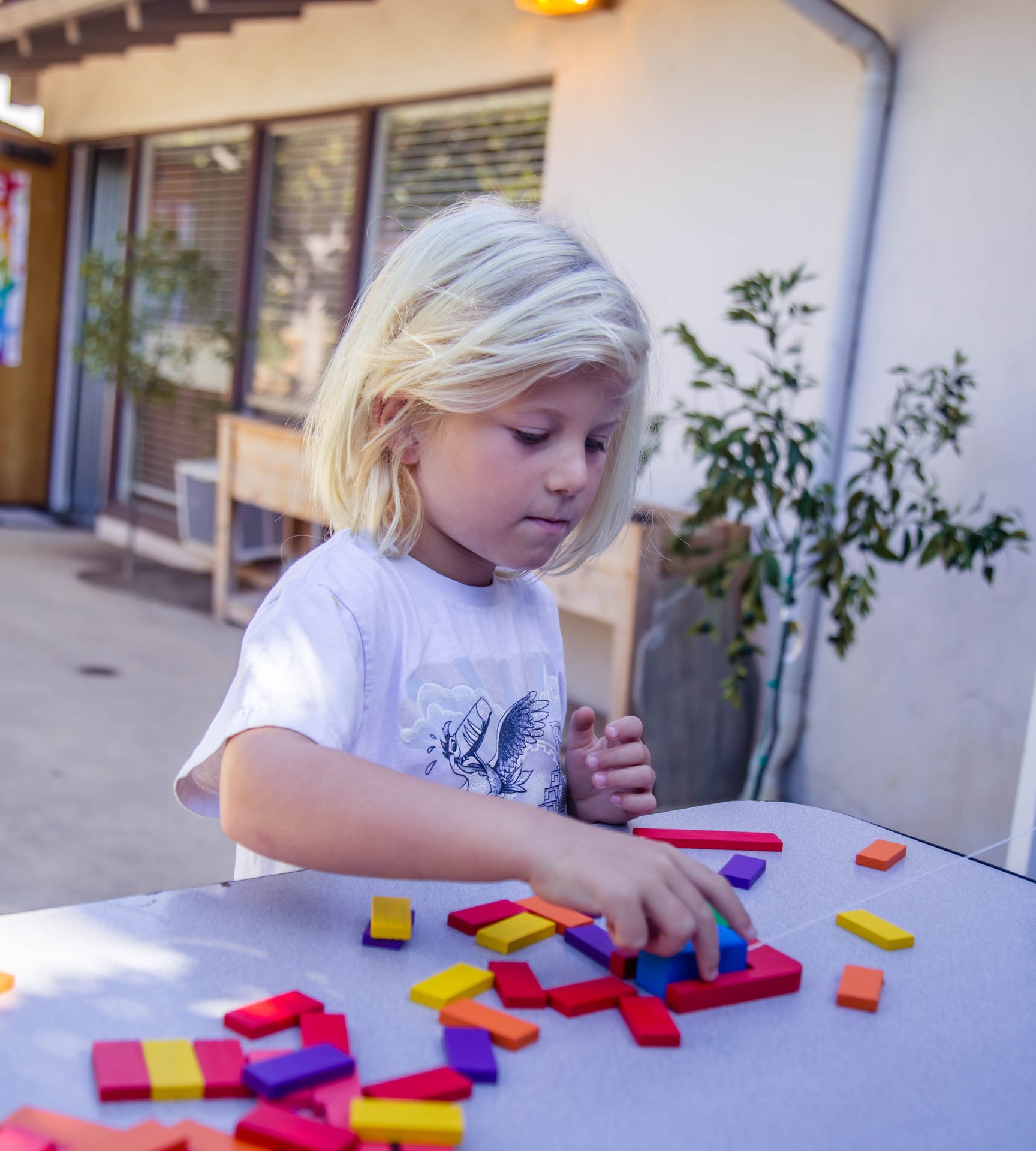 Young child arranging colorful wooden blocks on an outdoor table