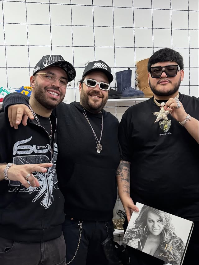 A woman in a patterned shirt and jeans sits on a chair against a solid orange background