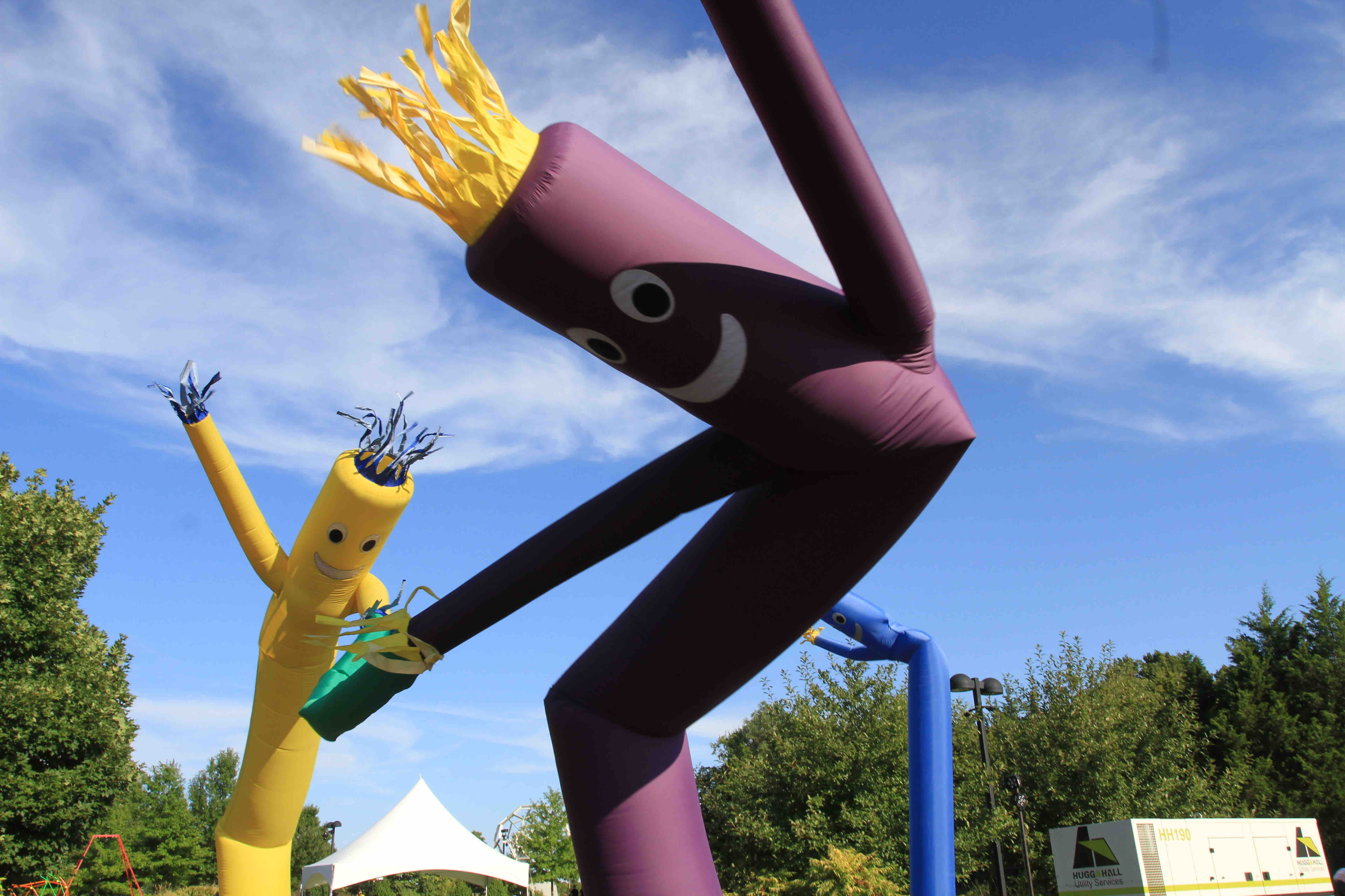 Colorful inflatable tube men dance in the wind against a clear blue sky.