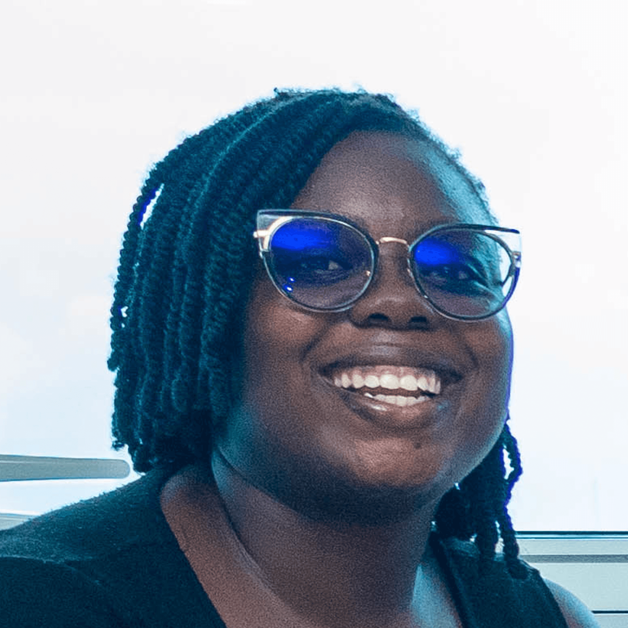 Smiling young woman with glasses and curly hair, wearing a striped top.