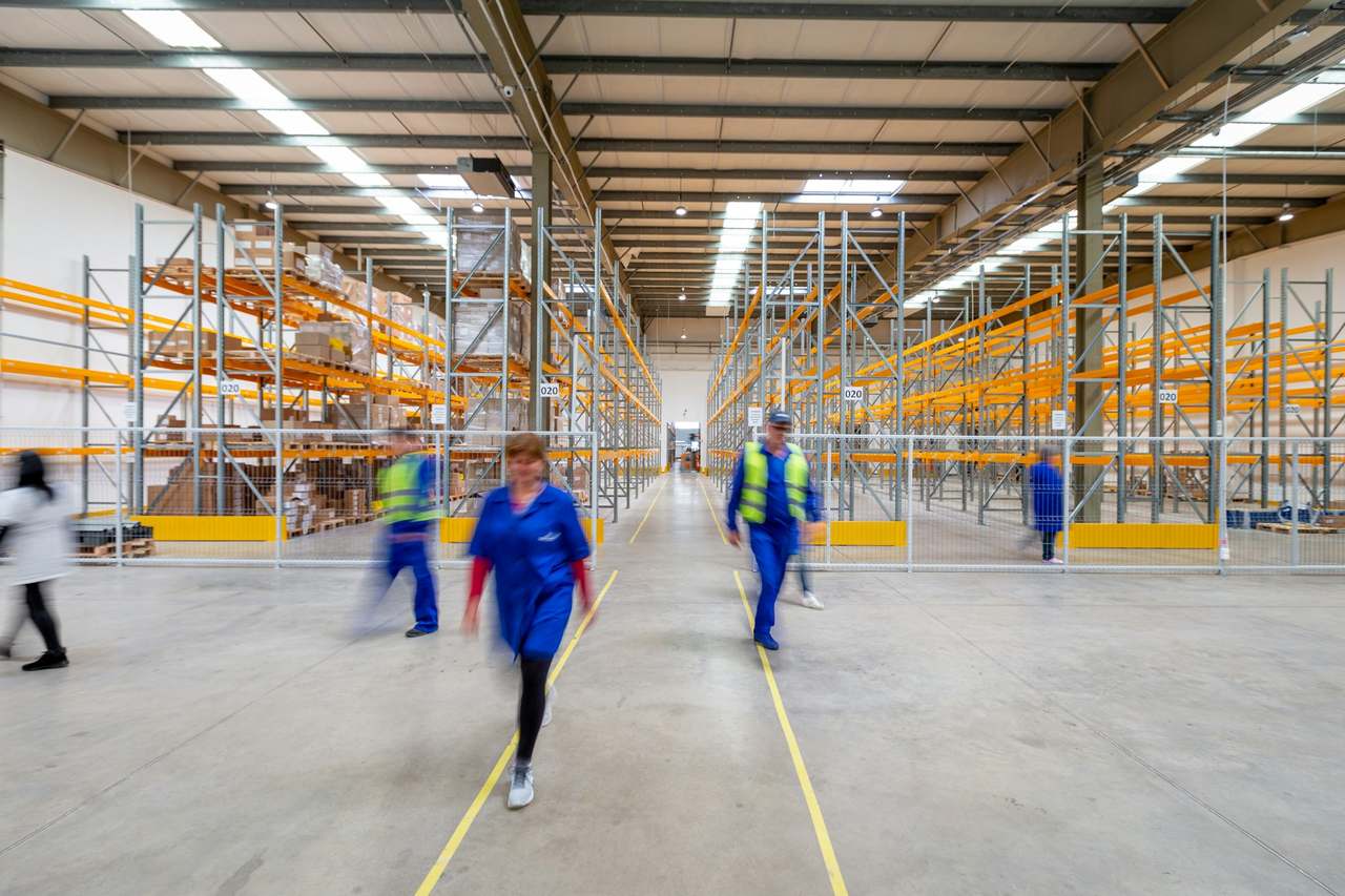 Workers walking through a bright warehouse aisle with pallet racking