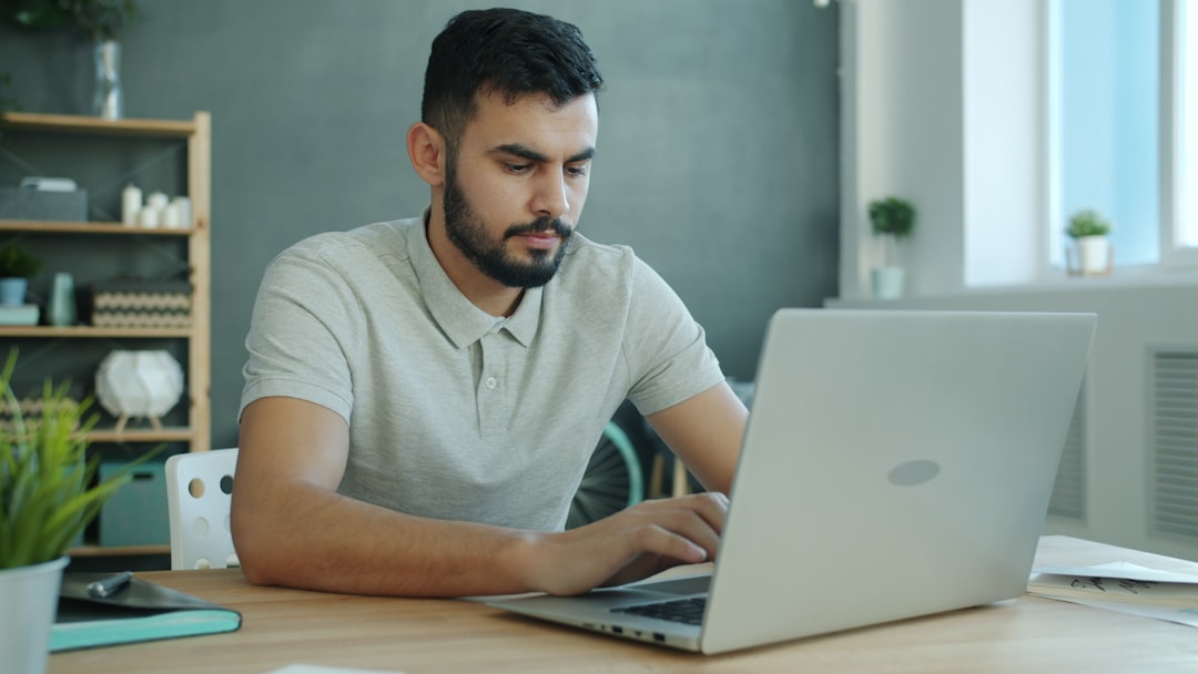A person is focused on working at a laptop in a modern office with shelves in the background, capturing a scene of concentration and productivity.