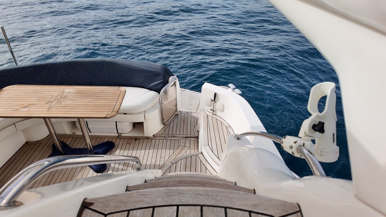 Sealine F37 aft cockpit and swim platform viewed from the flybridge — teak deck, fold-down transom door, stainless steel rails, and cockpit dining table with compass rose inlay, underway on open Mediterranean sea