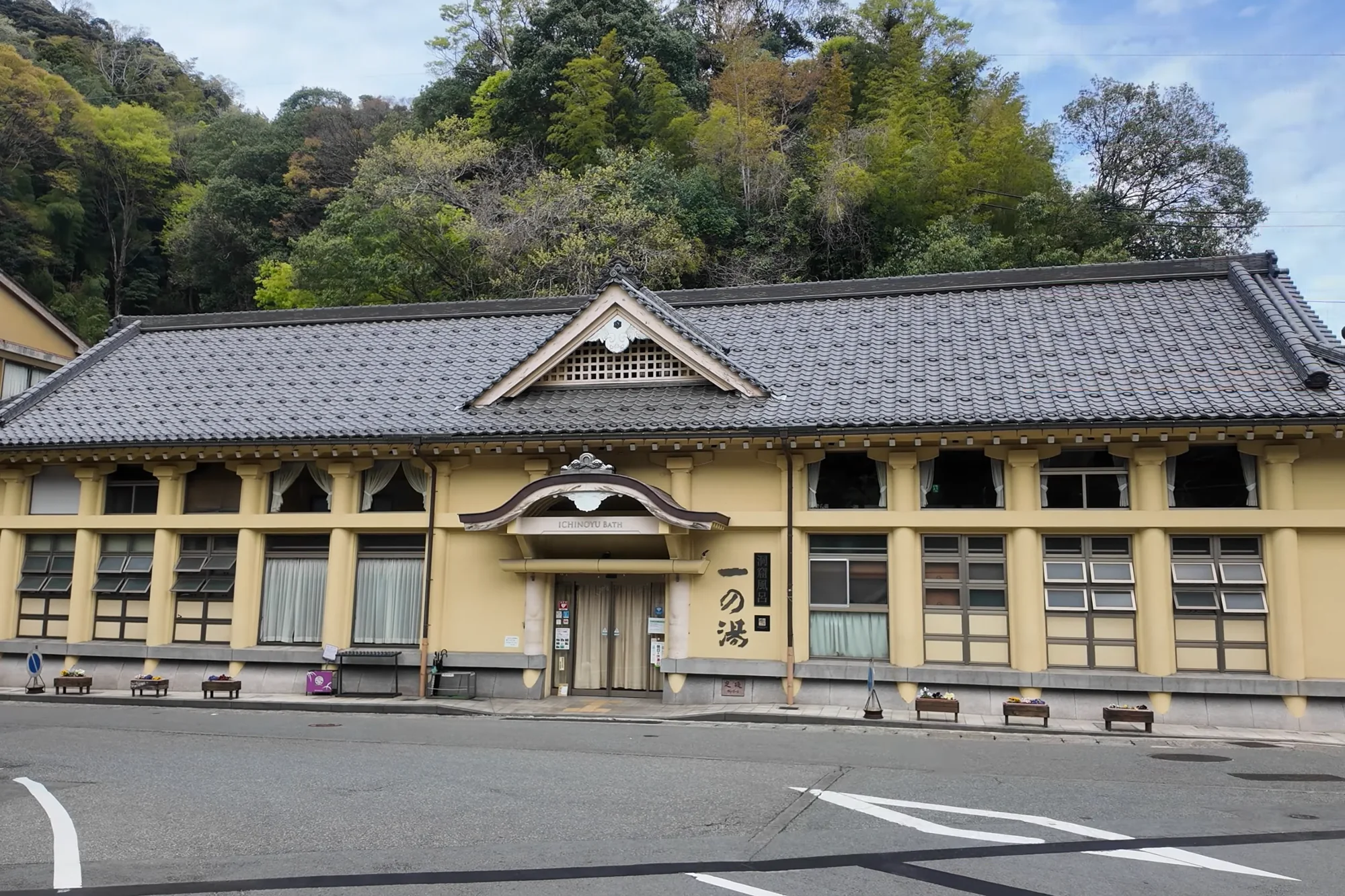 The pale-yellow hall of Ichi-no-yu bathhouse in Kinosaki seen in full from the street in spring.