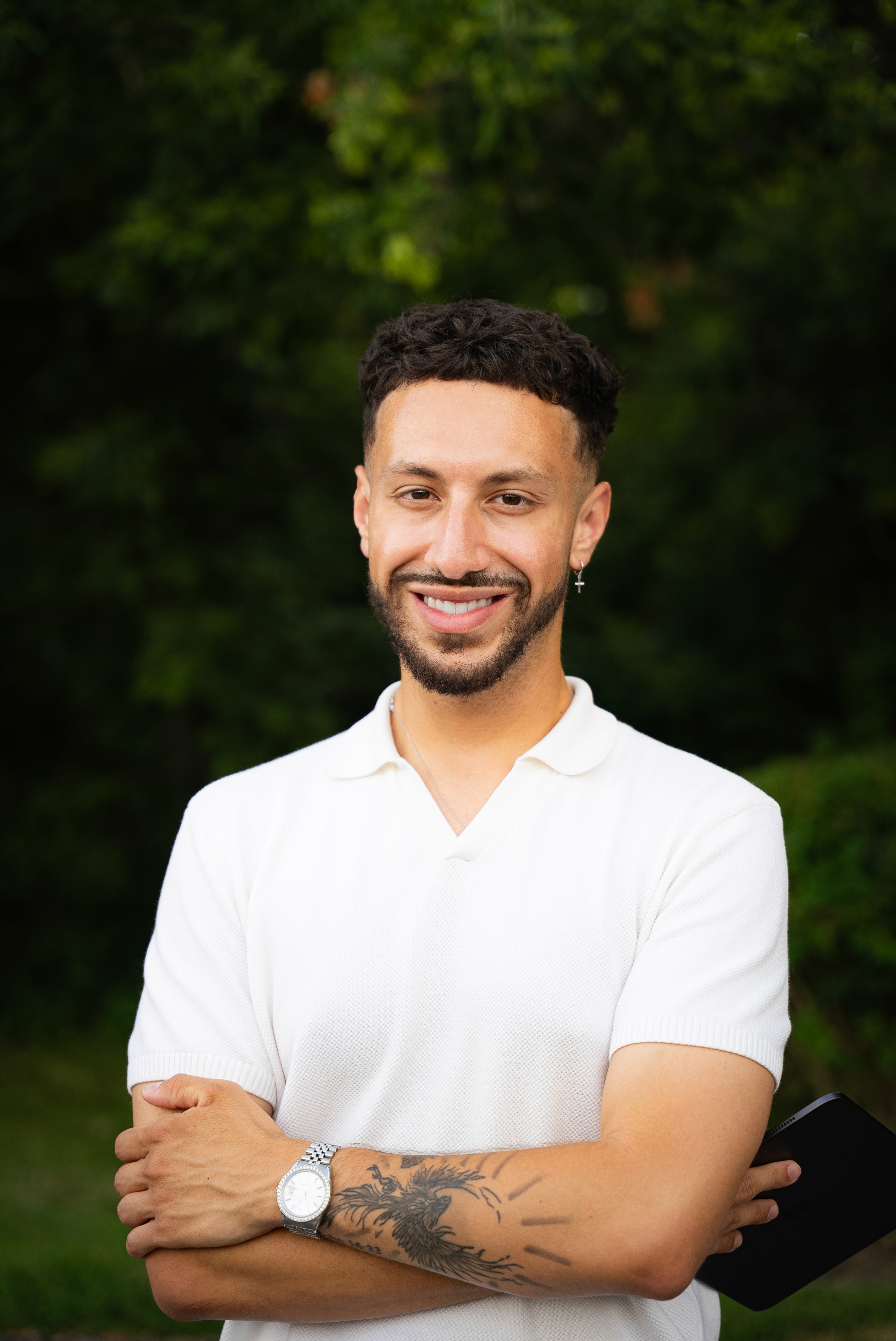 A man in a blue bomber jacket stands against a dark background. The lighting is dramatic, highlighting his focused expression. His pose is confident.