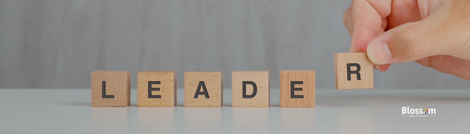 Wooden blocks spelling out the word 'LEADER' with a hand adjusting the final letter.