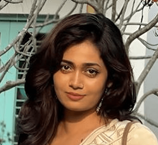 A woman with short curly hair wearing a black t-shirt looks into the camera.