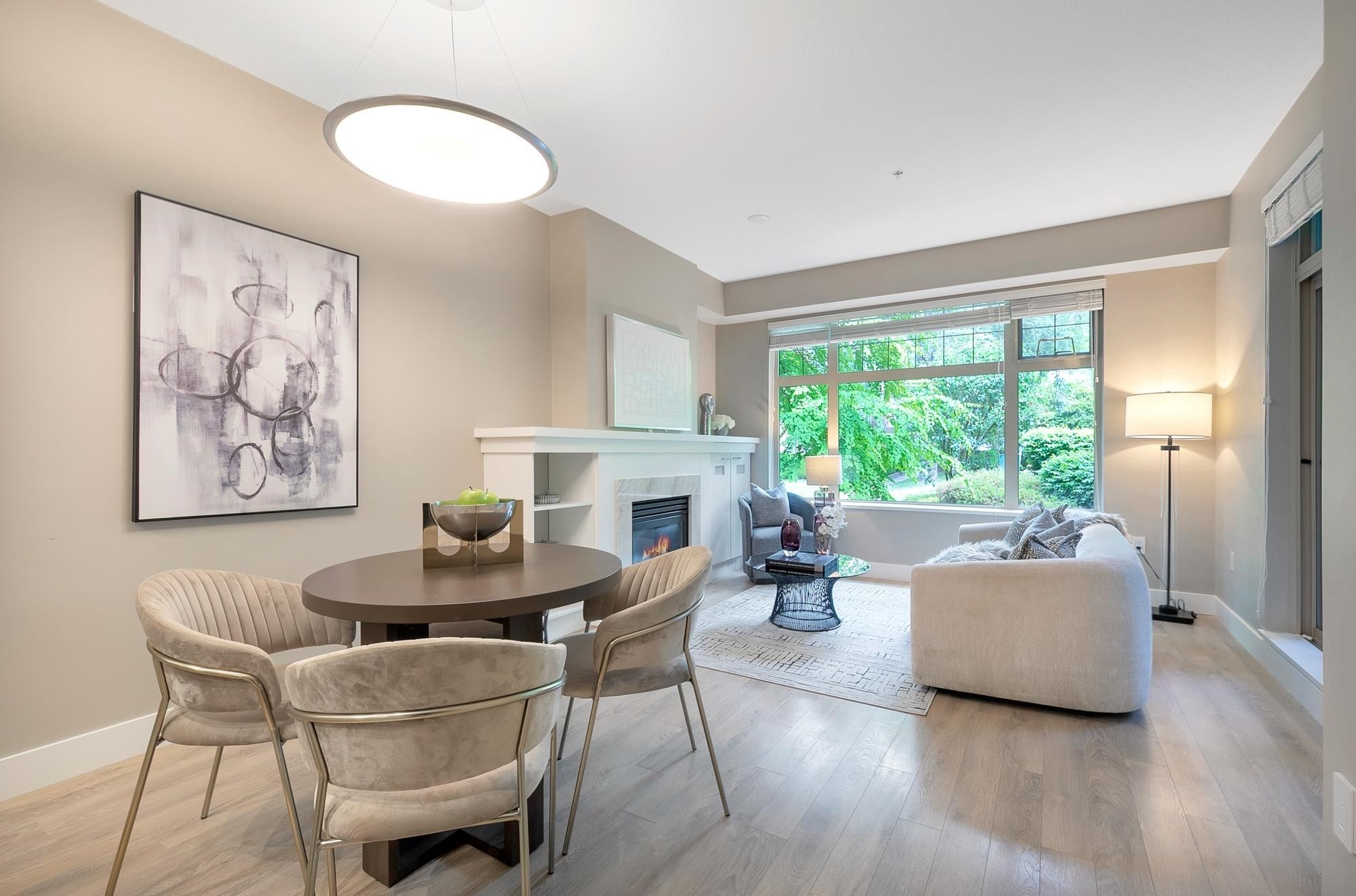 Bright, modern living room featuring a dining area, comfortable seating, and large windows with a view of greenery.