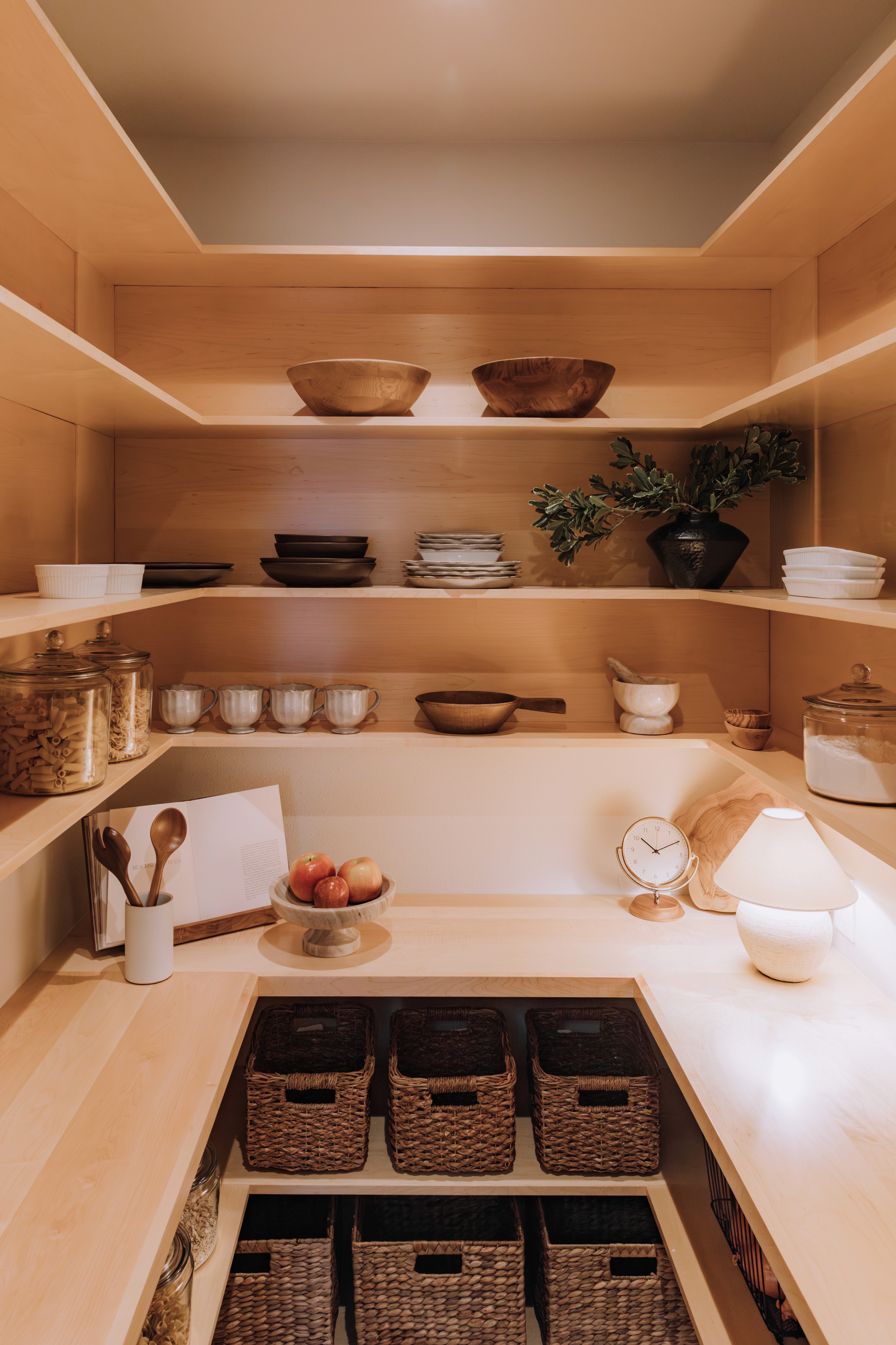 Custom pantry with pale wood shelves, marble counters, and woven baskets below.