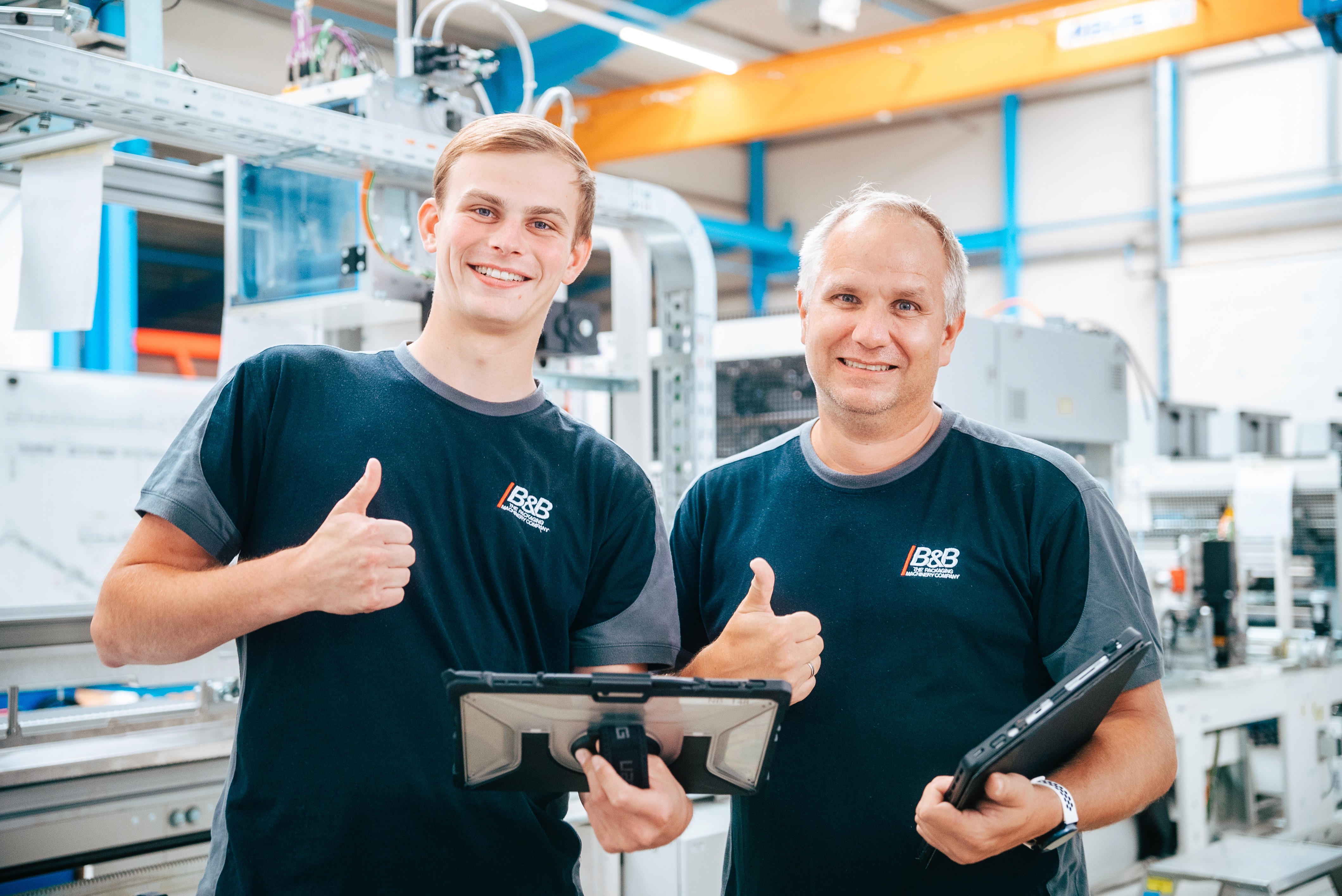Two happy employees in a production hall showing thumbs up. Teamwork and success.