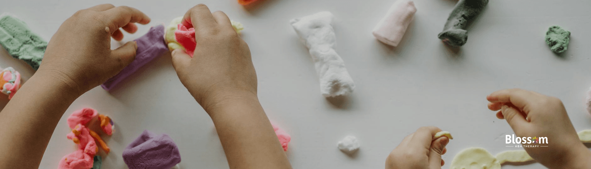 Autistic kids’ hands shaping colorful clay figures on a white table during ABA therapy in Georgia.