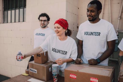 A group of volunteers in matching shirts organizes boxes outdoors, smiling and working together.