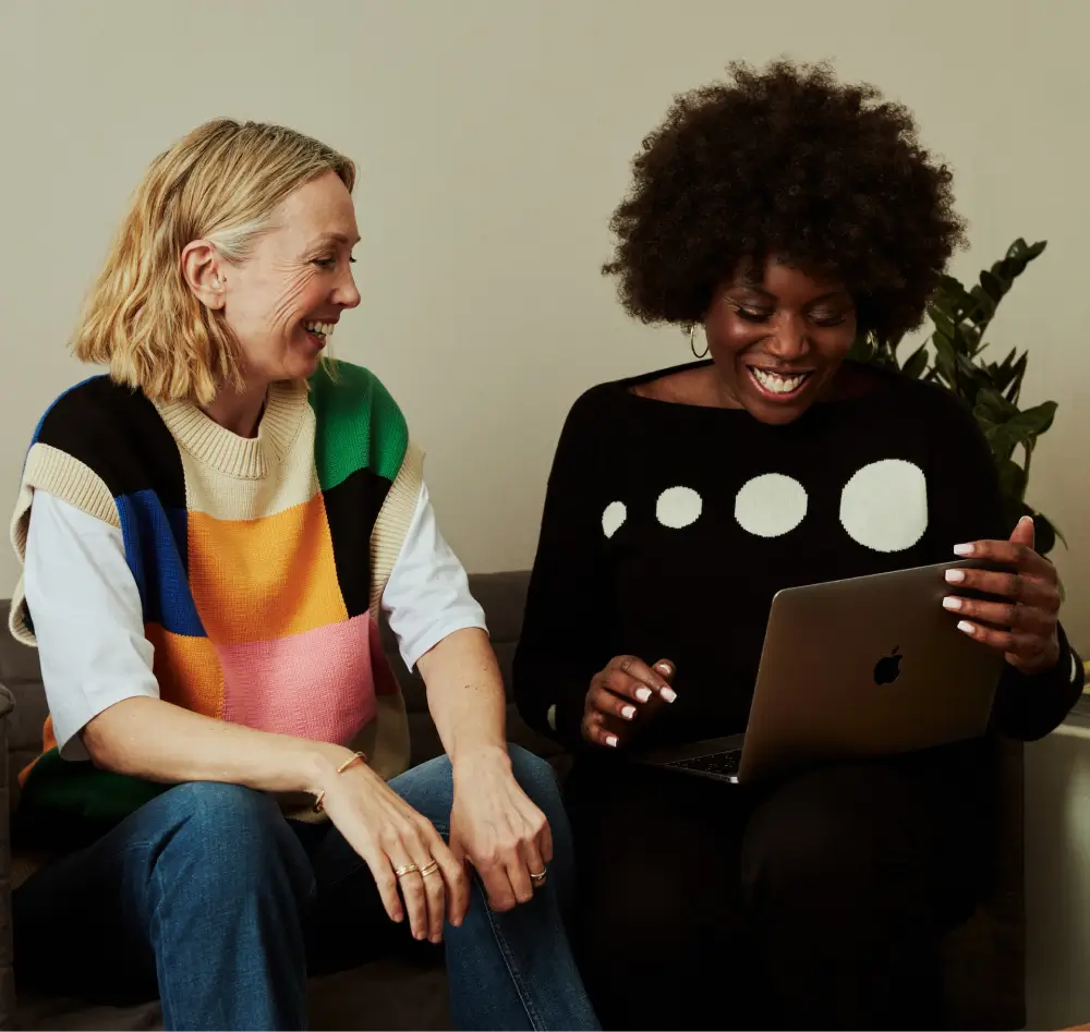 Photograph of two women seated on a sofa looking at a laptop screen