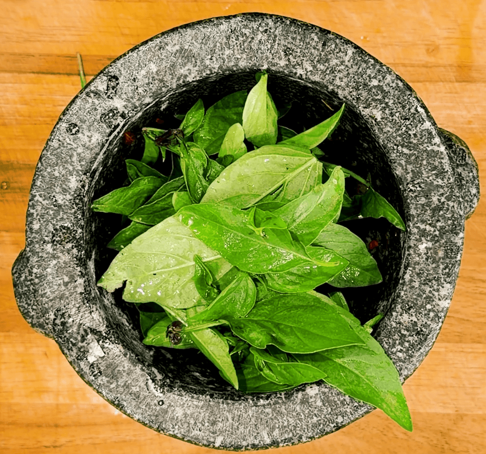thai basil overflowing a mortar and pestle about to be pulverized into a pesto