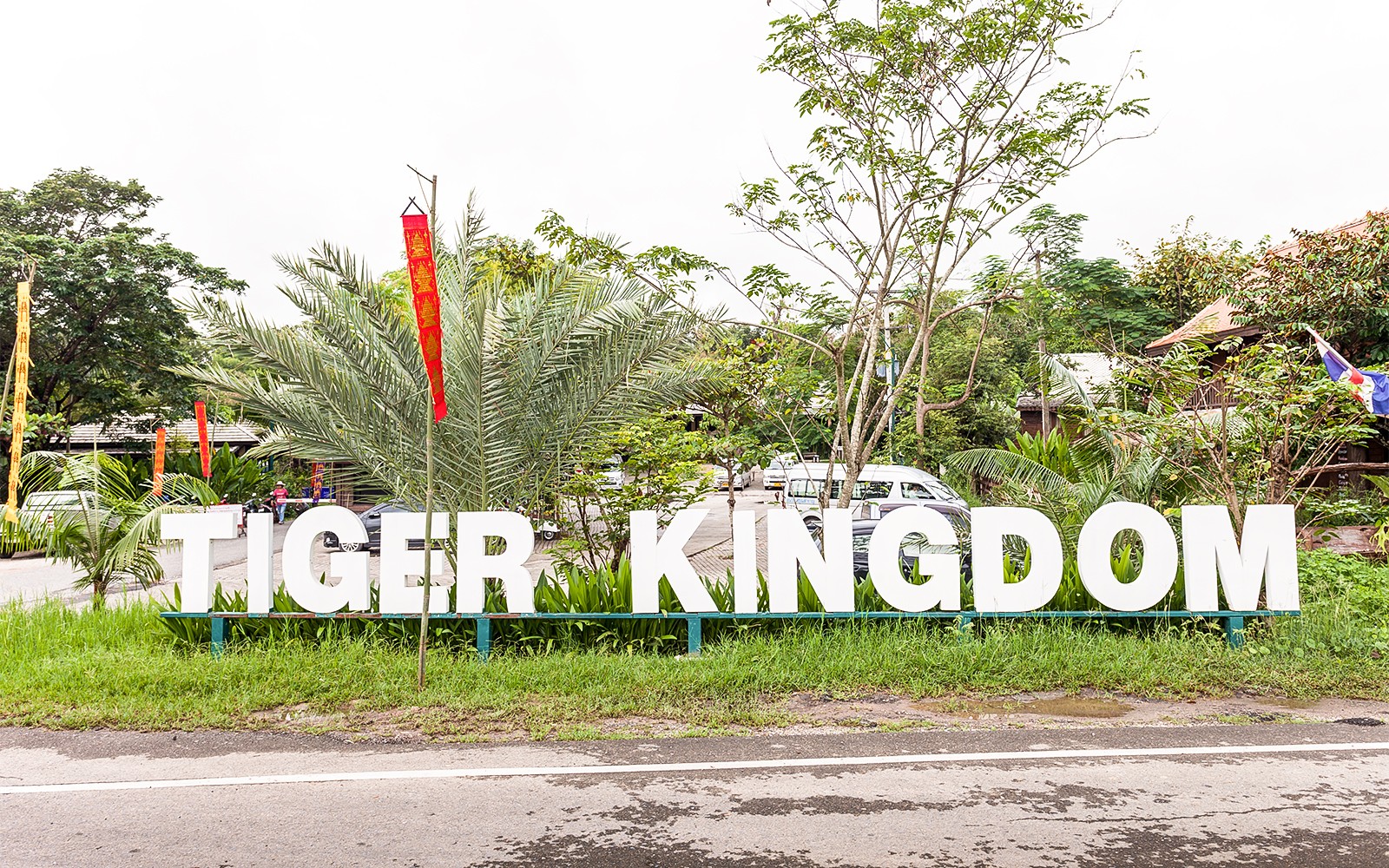 Placa de entrada do Reino dos Tigres cercada por vegetação e bandeiras.