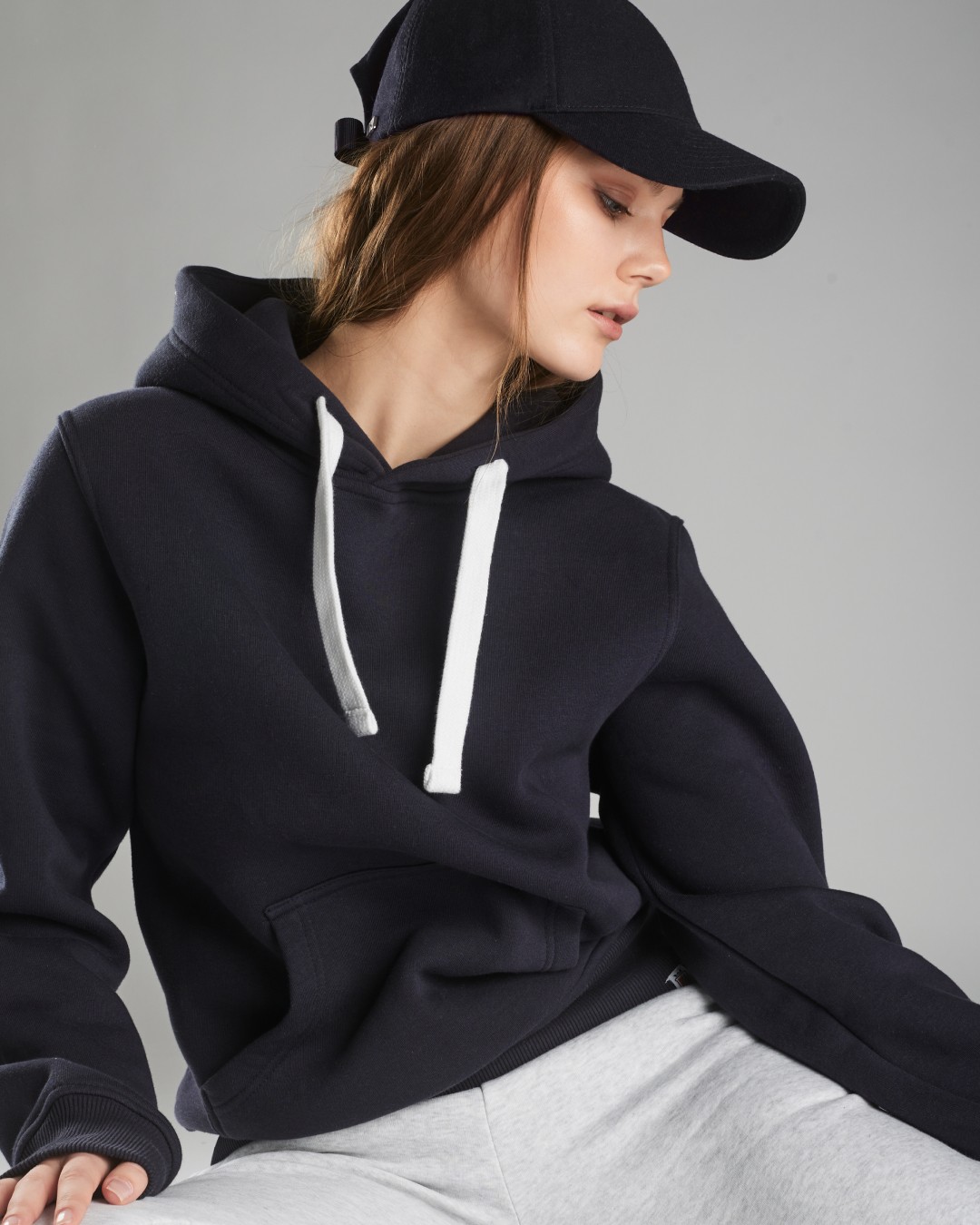 Woman wearing navy pullover hoodie and cap, relaxed fit, casual lounge styling.