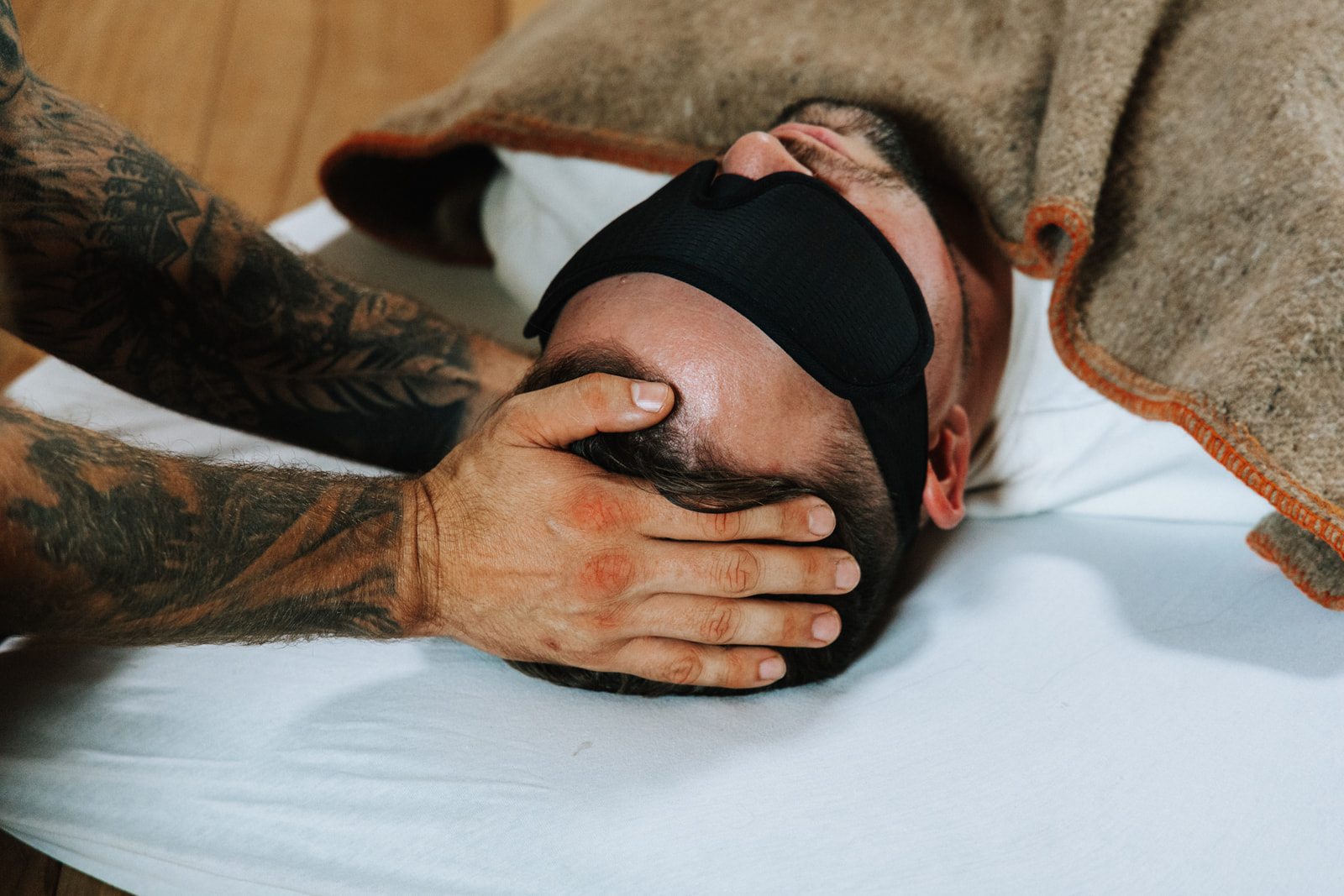 Begeleider houdt het hoofd vast van een deelnemer met oogmasker tijdens een geleide meditatie