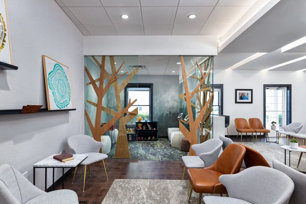 Modern waiting area with white walls, stylish furniture, plants, and a large window letting in natural light.