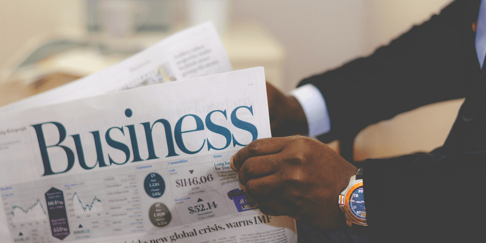 Person in suit holding business newspaper with financial charts and market data visible.
