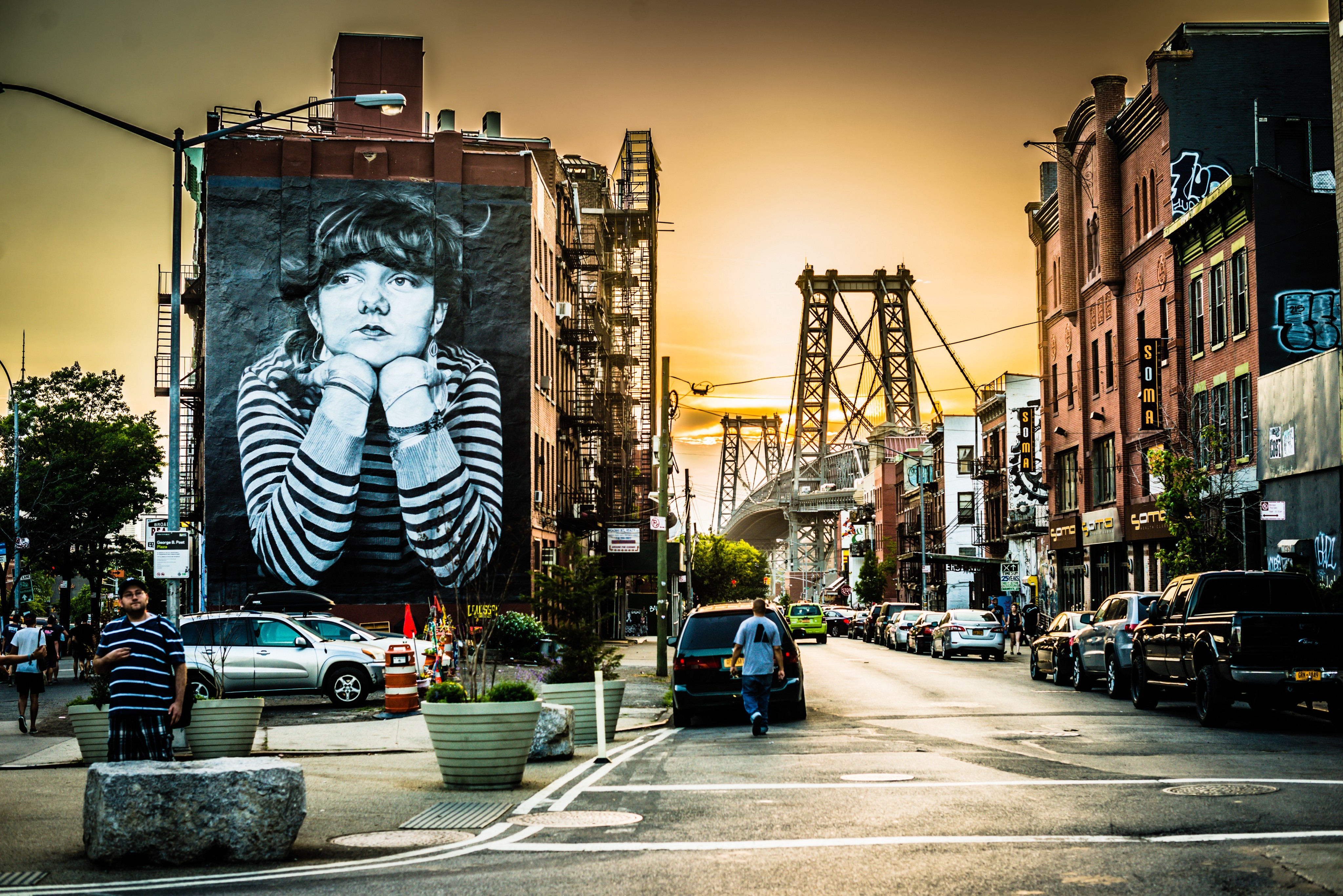 Street scene in Williamsburg at dusk, with cars and a large mural in the background.