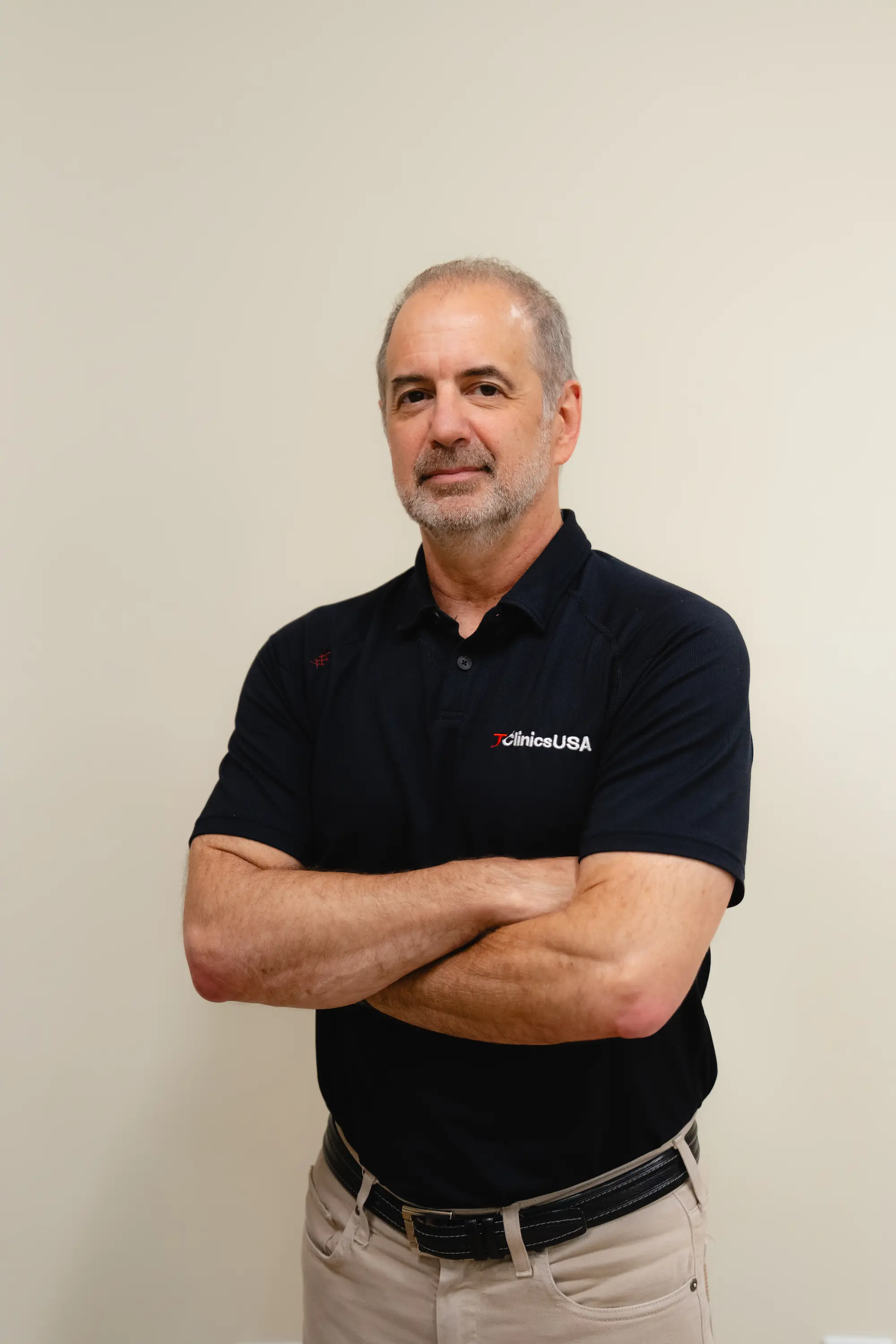Portrait of a man in a black polo and khaki trousers with arms crossed