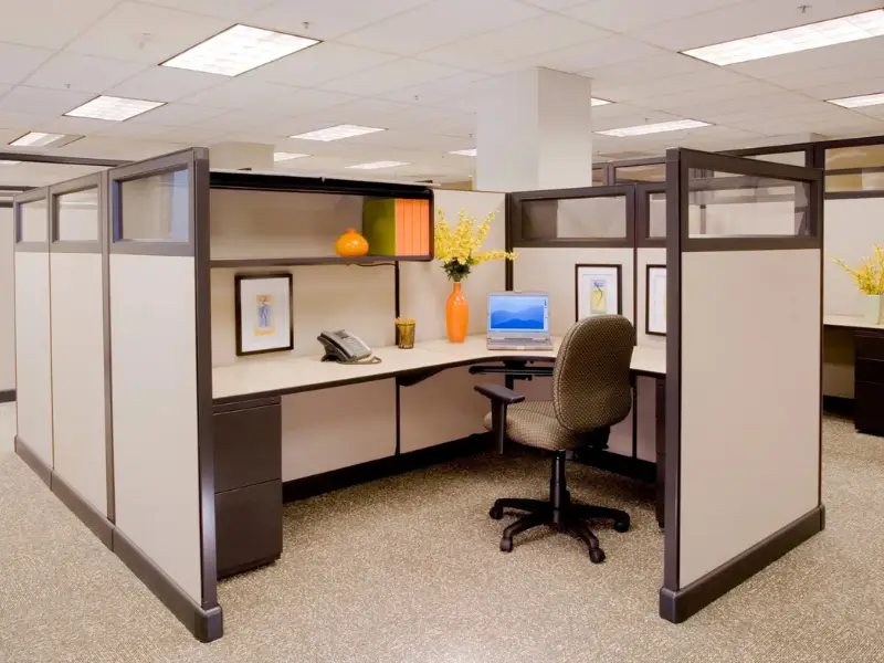 Modern office cubicle workstation with laptop, ergonomic chair, and decorative desk items.
