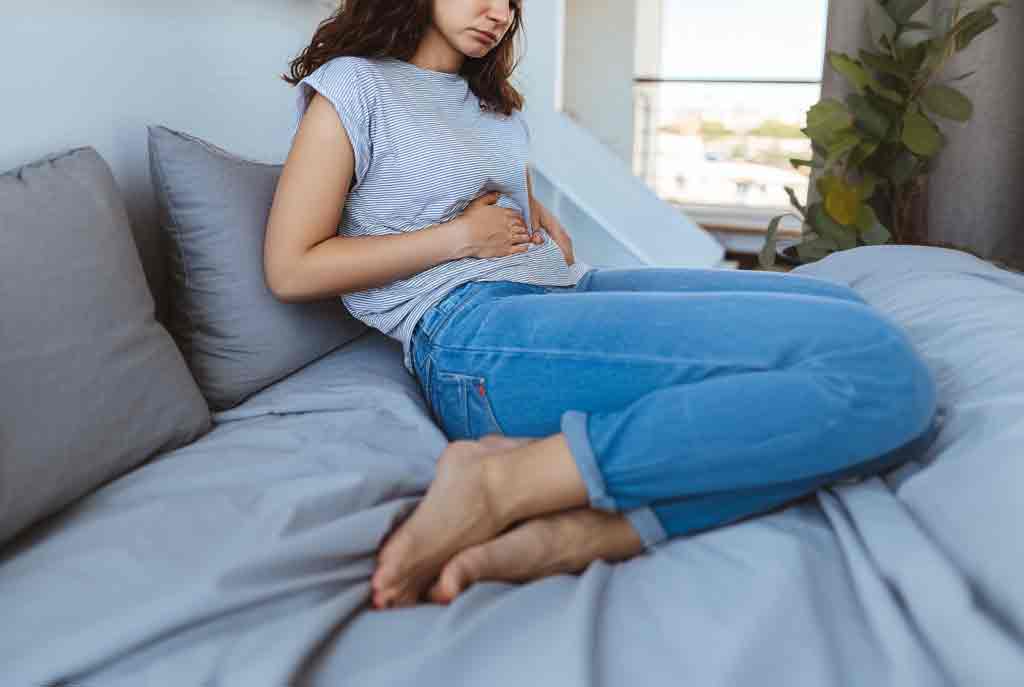 Eine junge Frau fasst sich vor Schmerzen an den Bauch