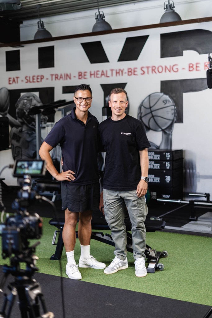 Behind-the-Scenes Foto aus einer Produktion bei einem Kunden. Zu sehen ist der Kunde (links) und Inhaber von Damm Media (rechts) nebeneinander im Sportstudio des Kunden.