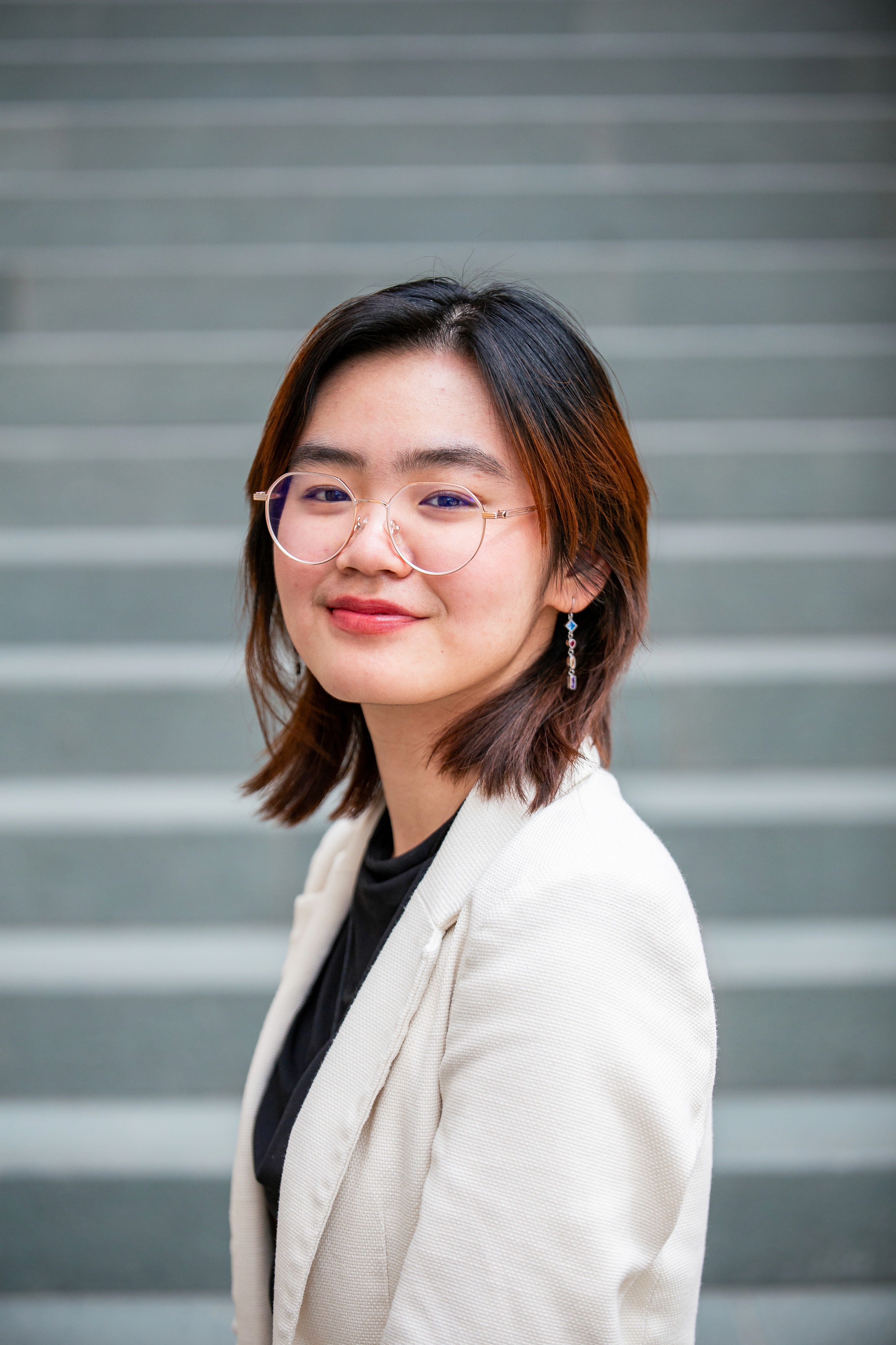 Headshot of Natasha, dressed in a white suit and black top with round glasses, smiling at the camera