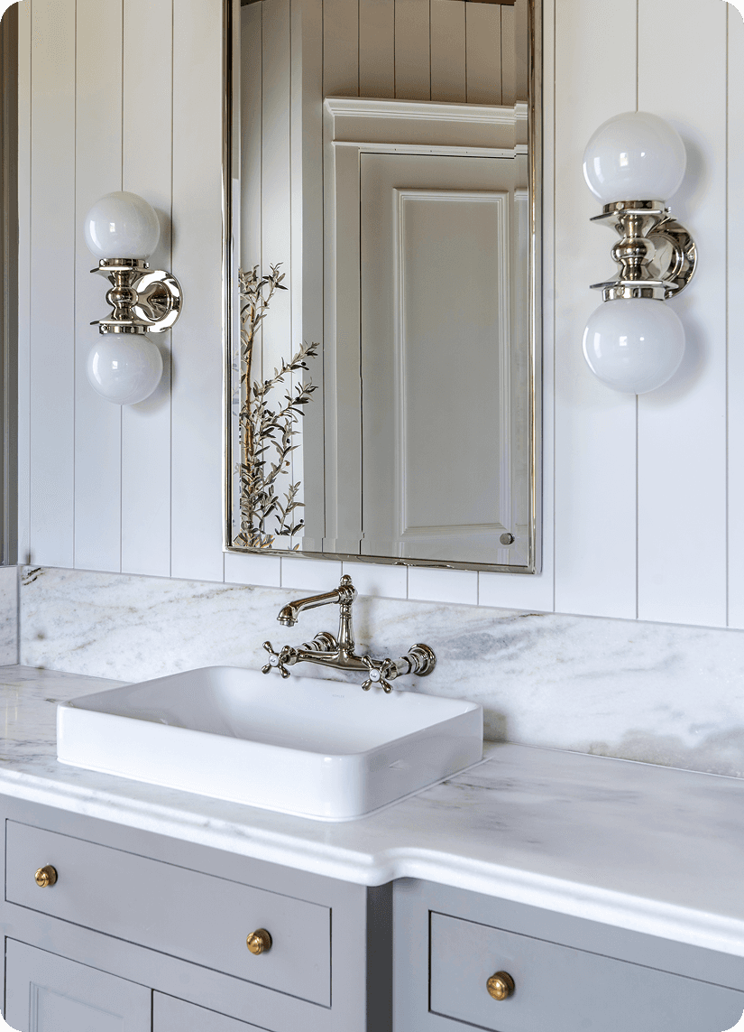 Elegant bathroom vanity with white marble countertop, vessel sink, brass wall-mount faucet, and globe sconce lighting
