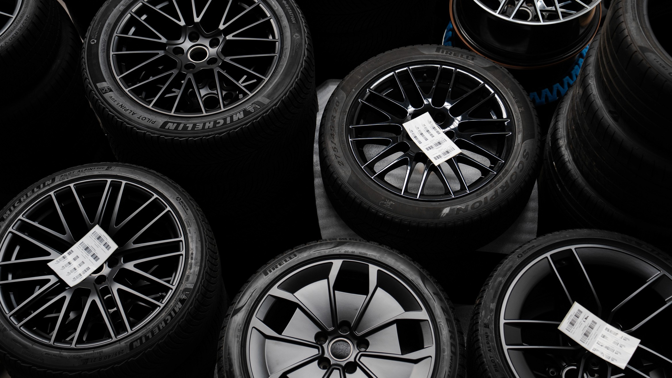 Mehrere schwarze Kompletträder mit montierten Reifen, sauber aufgereiht und mit Etiketten versehen – fotografiert in einer Werkstatt oder Lagerumgebung.