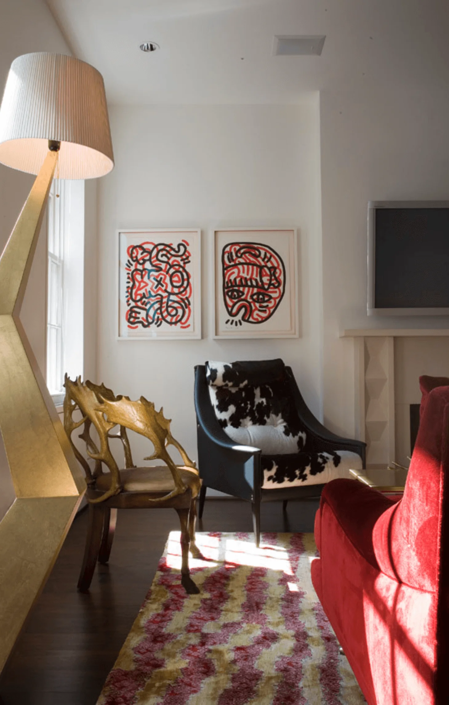 A gilt antler chair and black leather armchair with cowhide accents sit beneath two graphic prints in this Greenwich Village living room