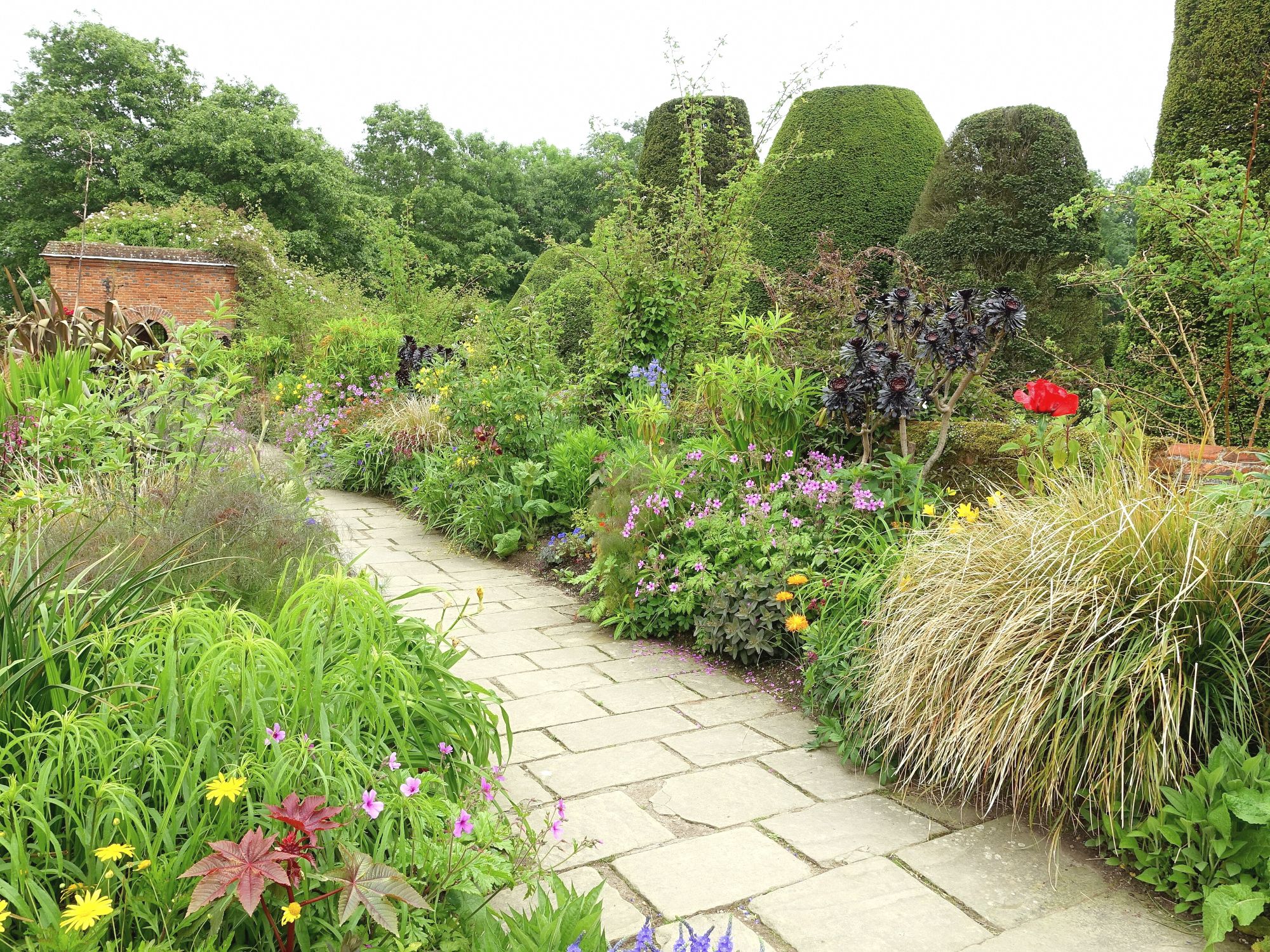 A stone path through deep borders of flowering perennials