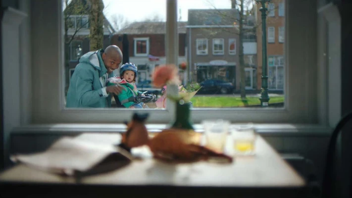 A man pointing trough a window with his daughter on a bike