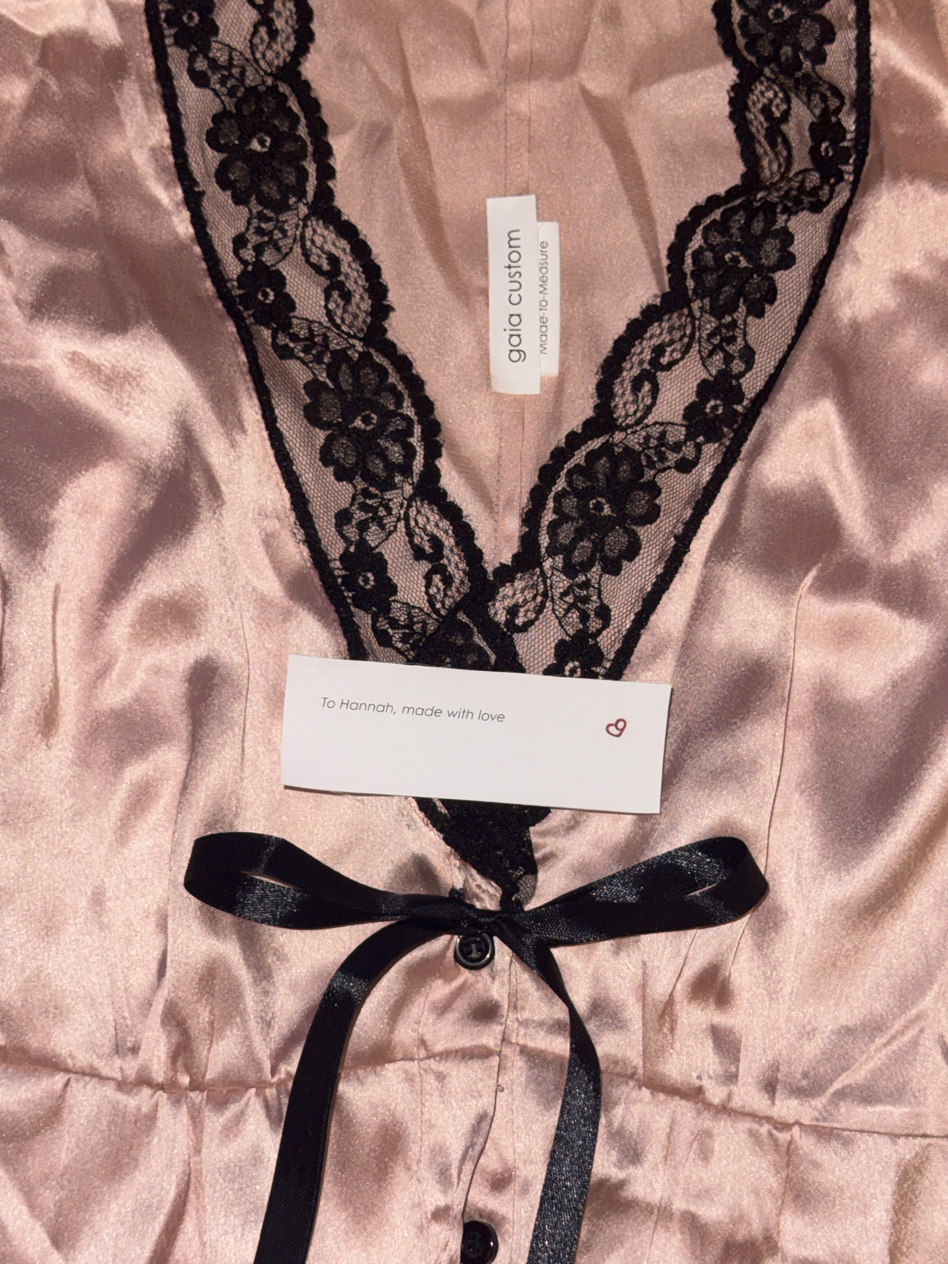 Close-up of blush satin bodice with black lace V-neck trim, centre ribbon tie, and soft quilted texture
