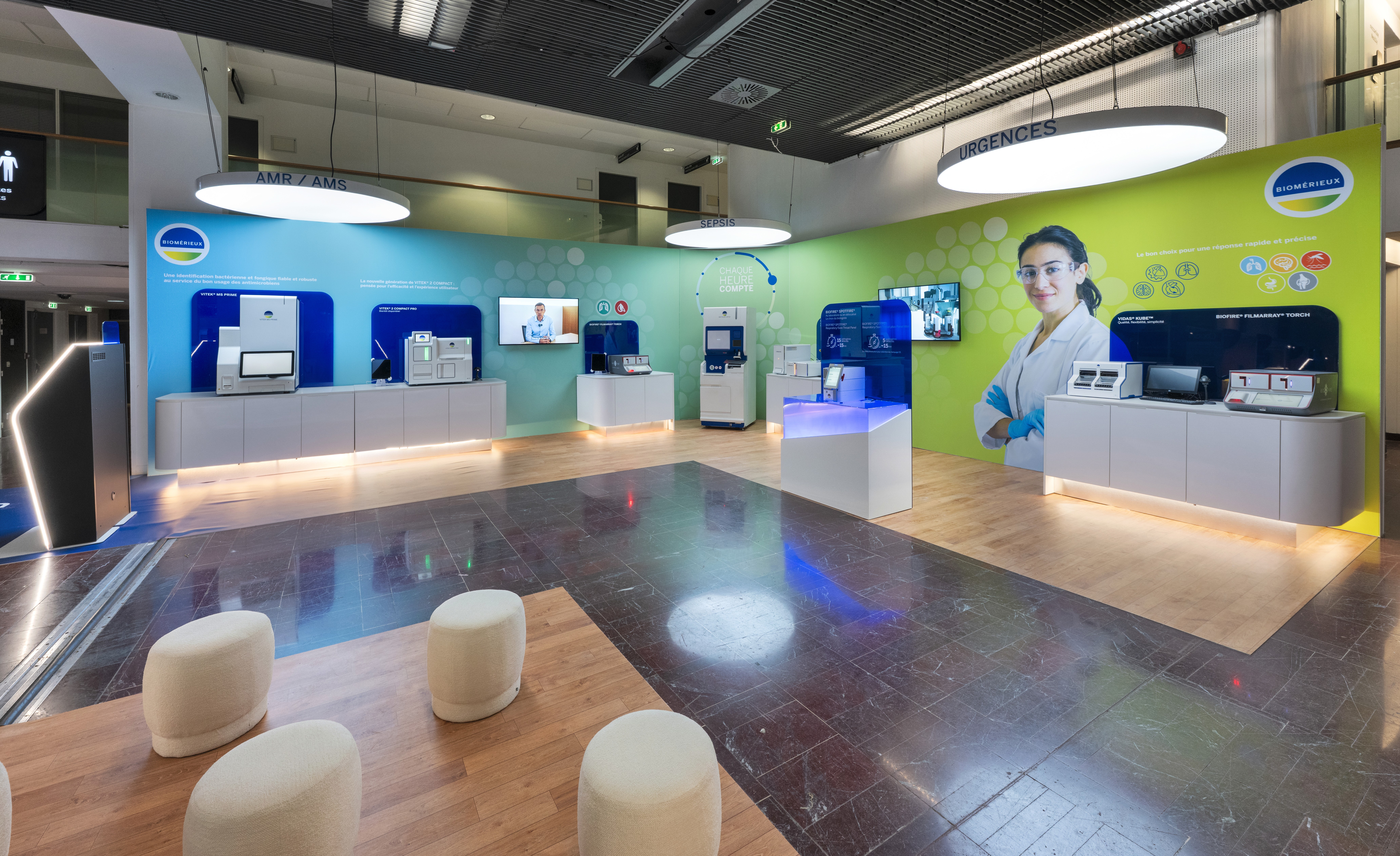 Stand bioMérieux RICAI 2025 conçu par Expace – vue entrée du stand avec drapeau logo rétroéclairé monumental, comptoir d'accueil arrondi et aperçu des zones diagnostic en arrière-plan