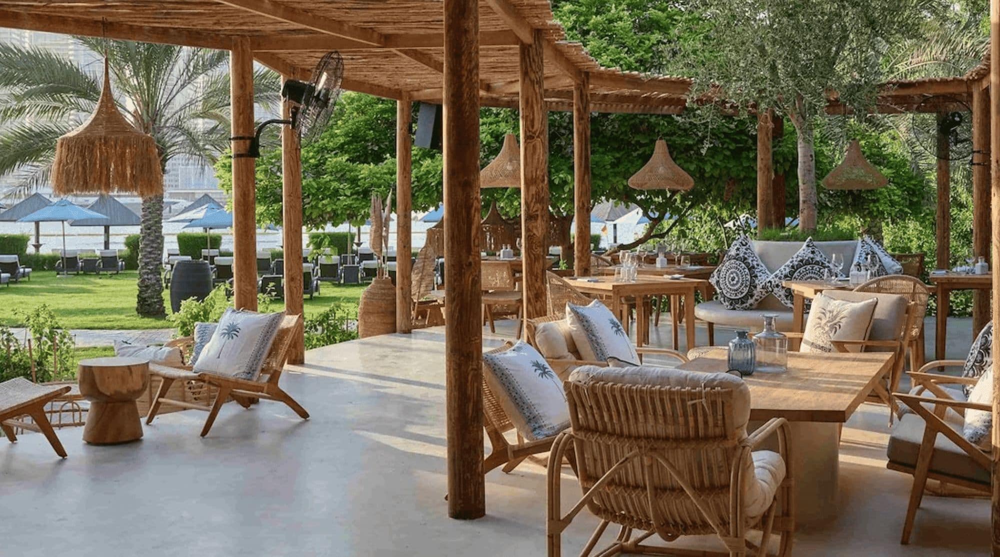 A beach restaurant in Dubai that features open spaces for dining, wooden tables and chairs, and tons of greenery.