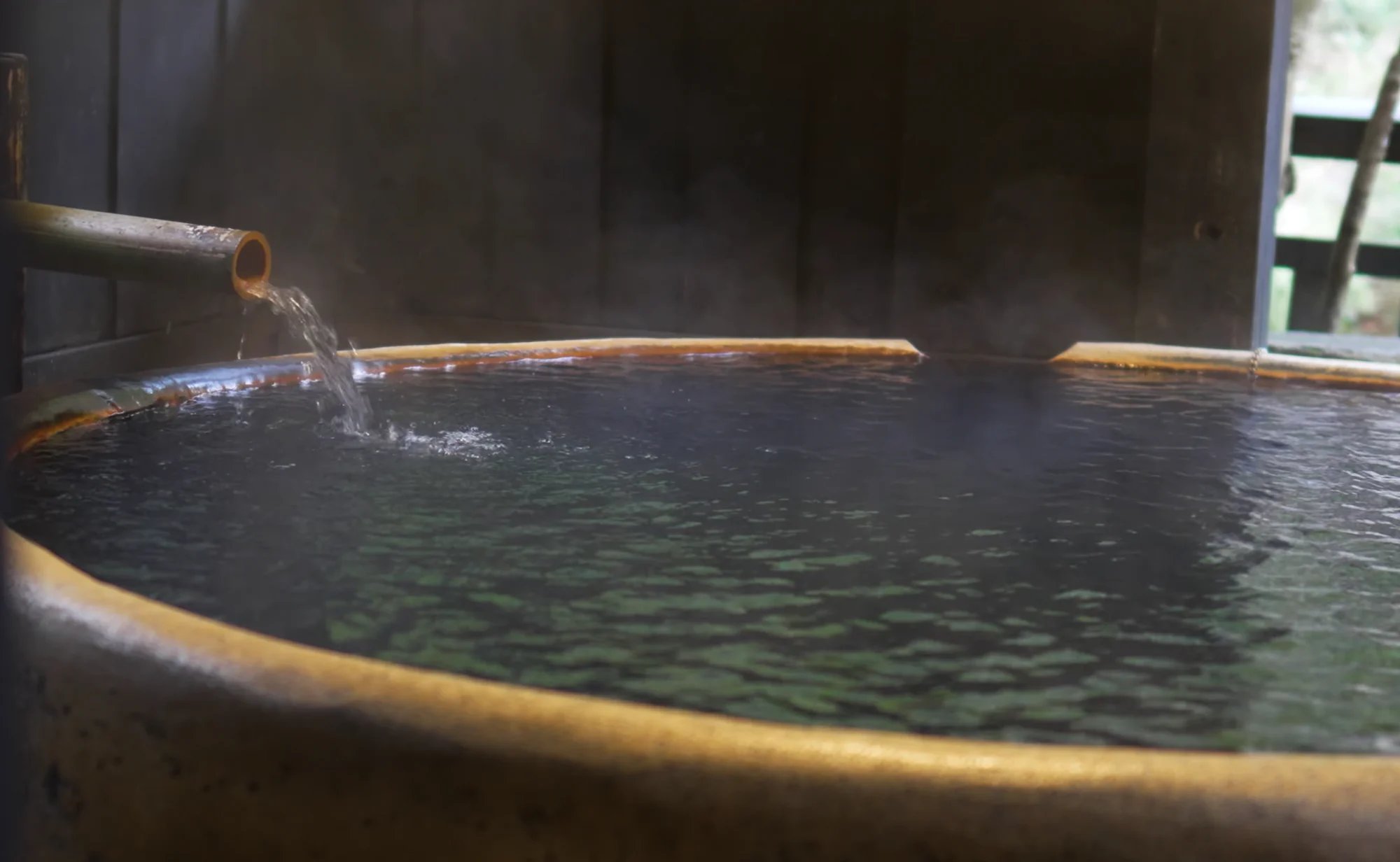 A round private hot spring tub with bamboo spout open to winter forest