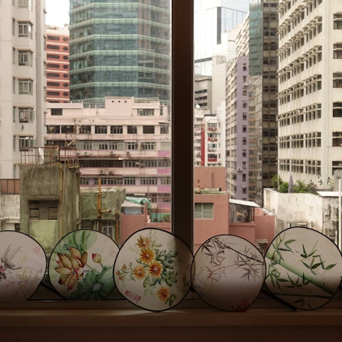 装饰扇子上有花卉和竹子图案，被放置在俯瞰高楼大厦的窗台上。