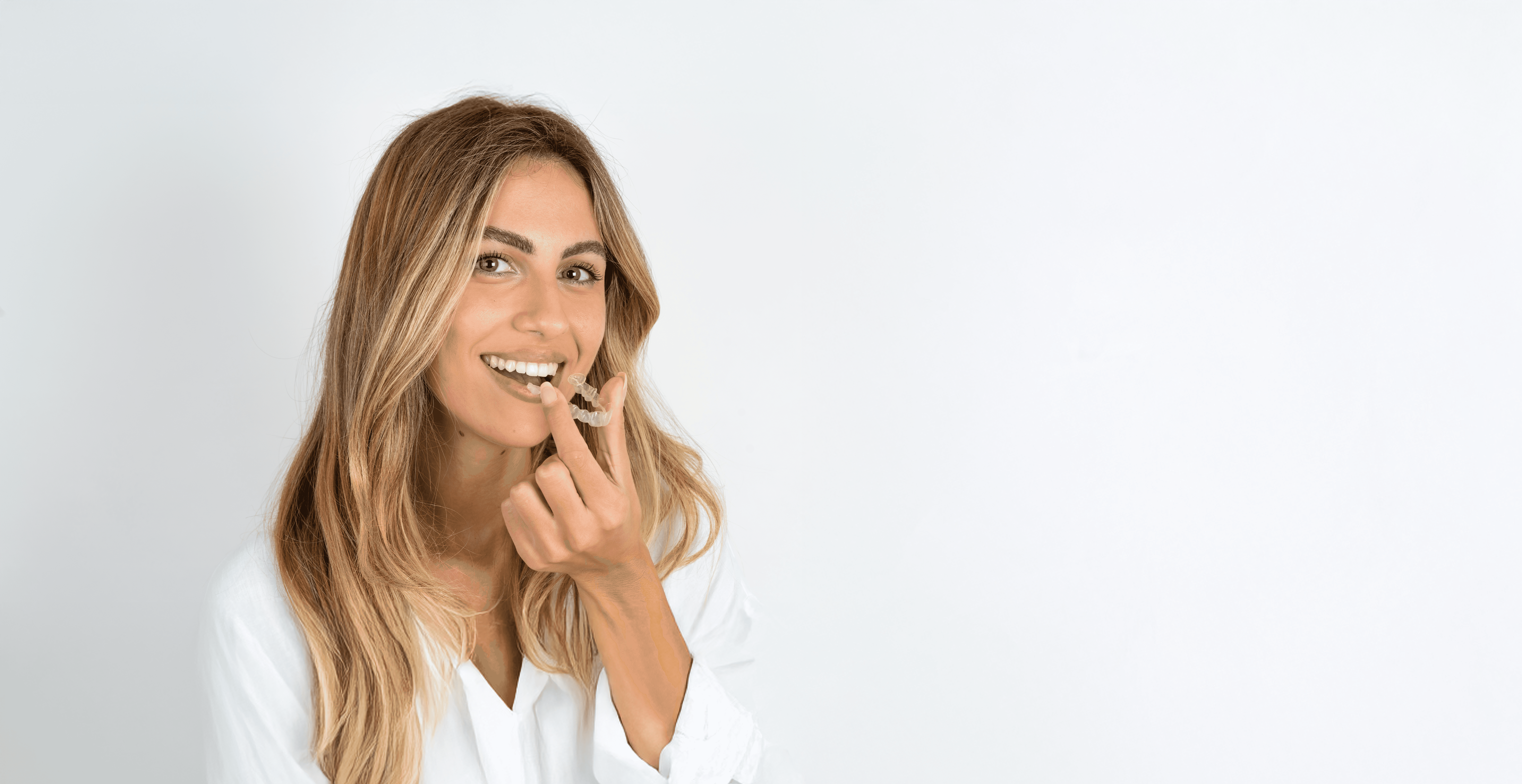 A woman smiles and holds invisalign clear aligners with a case, showcasing a certified invisalign provider at Bella Medical Centre