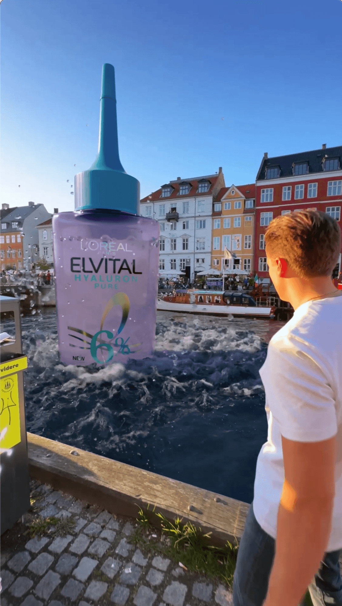 A giant L'Oréal Elvital bottle rising from a city canal as a man watches from the dock