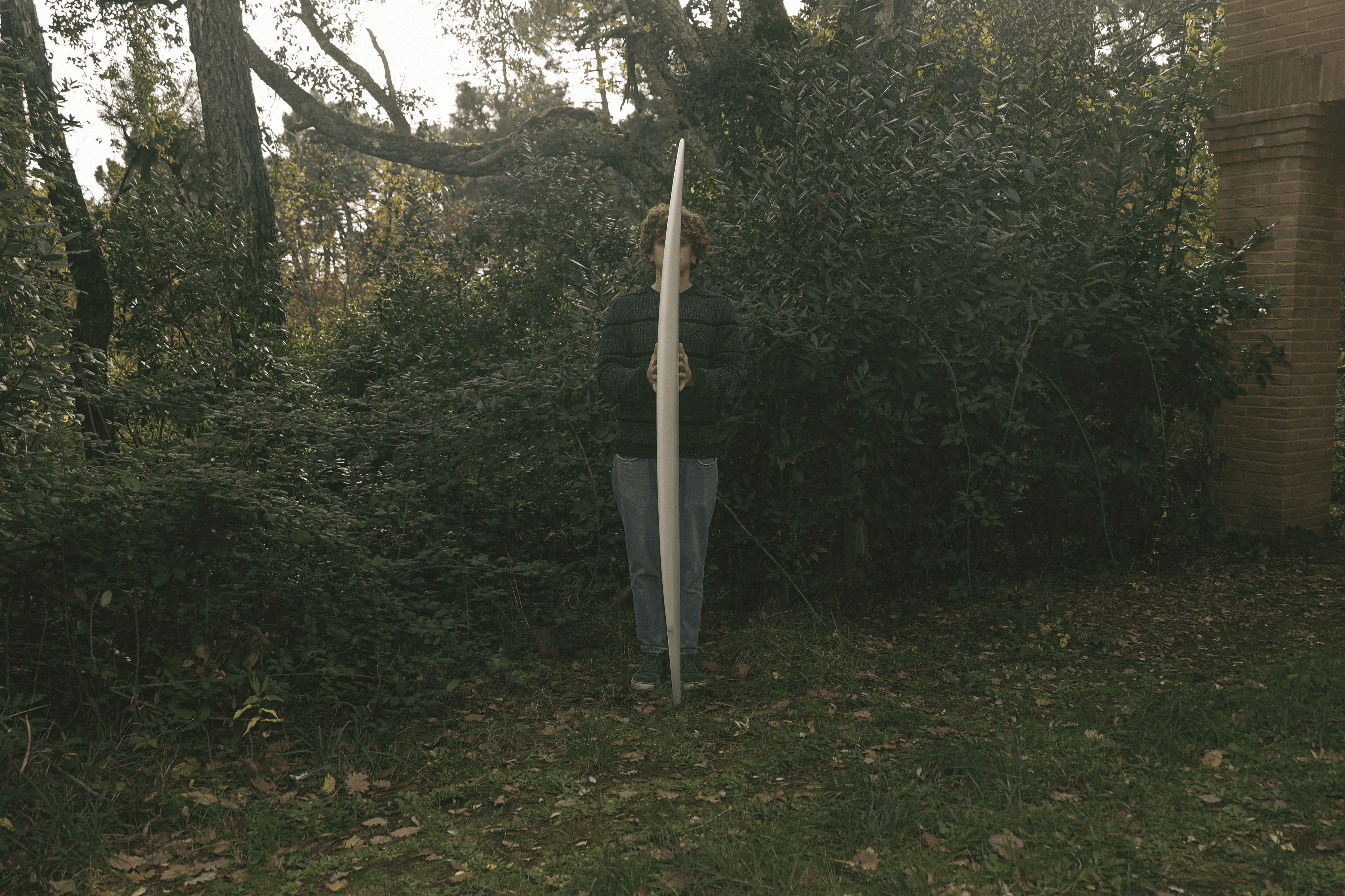 Una persona in piedi coperta da una tavola da surf Blue Java stretta e chiara, nel mezzo di una fitta vegetazione verde.