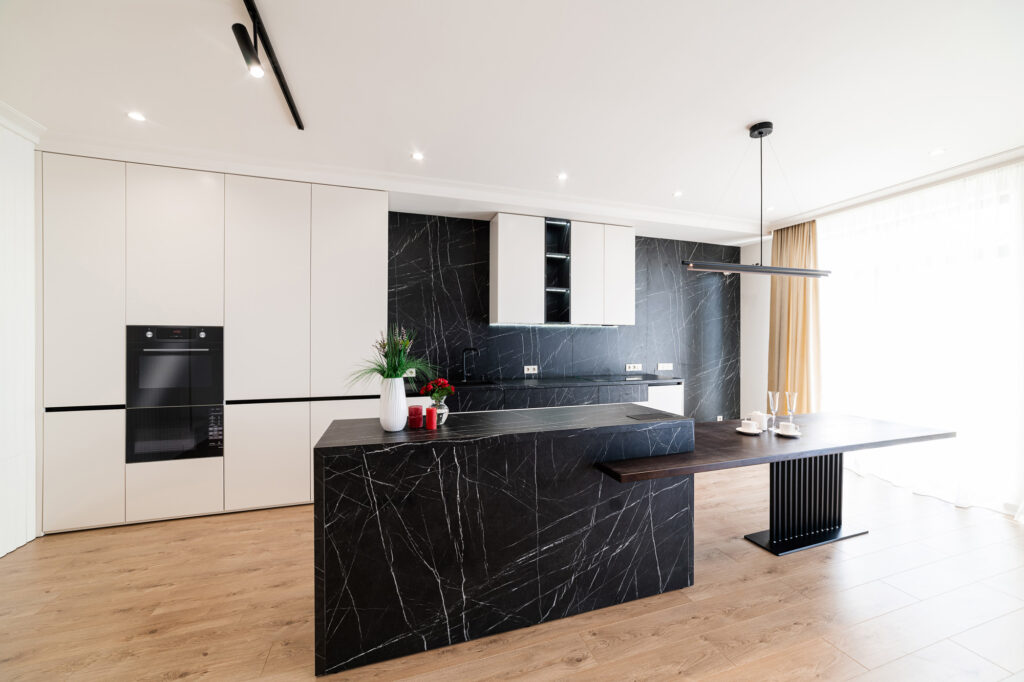 Contemporary condo kitchen remodel by B&Y Reno Corp featuring matte black marble island and backsplash with integrated dining counter, surrounded by clean white cabinetry and built-in appliances