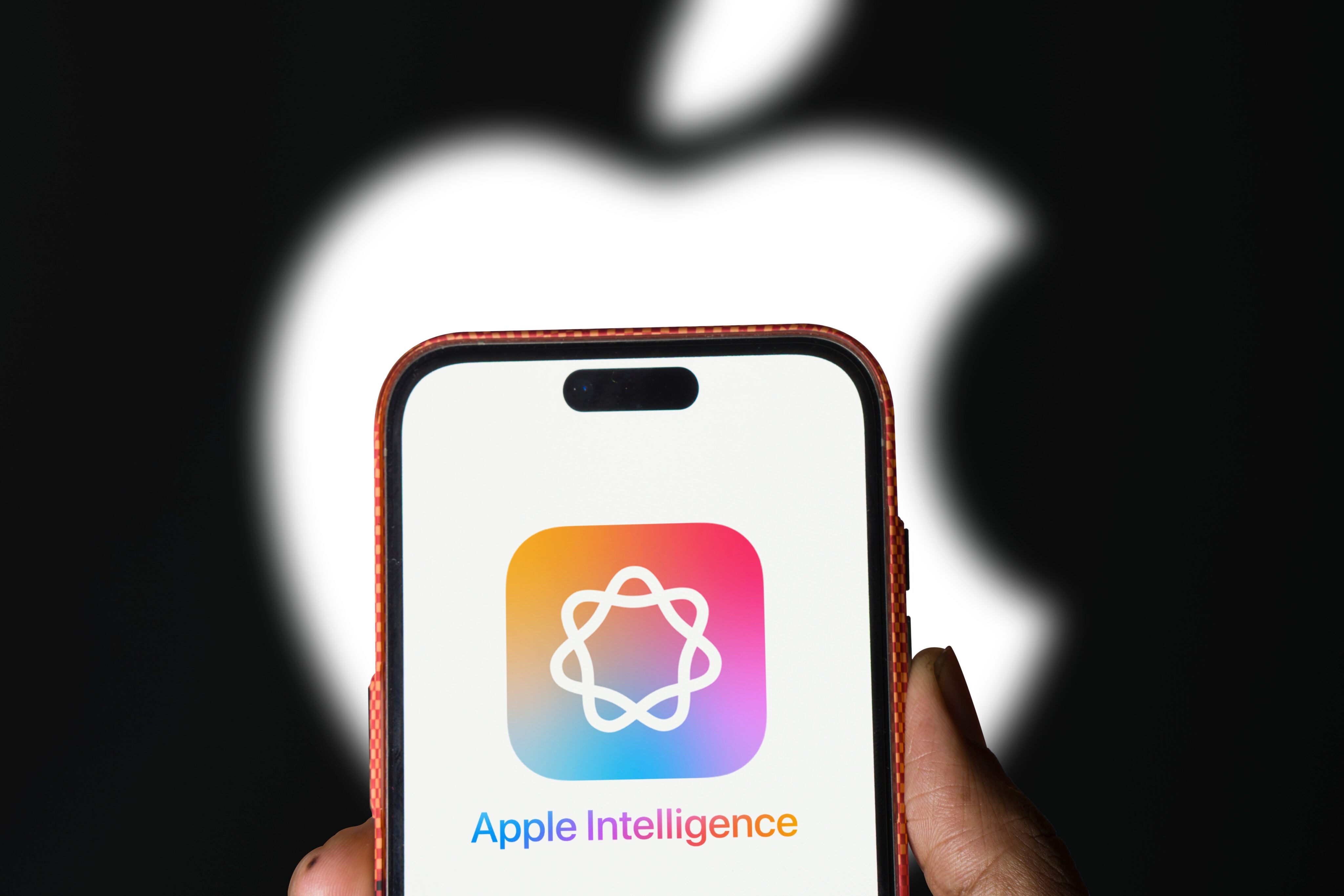 A hand holding a smartphone displaying the Apple Intelligence logo on its screen, set against a black background.