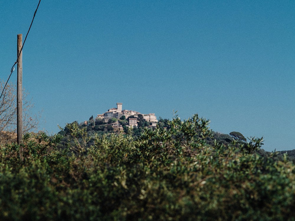 A distant view of a hilltop structure against a clear blue sky, surrounded by lush greenery.